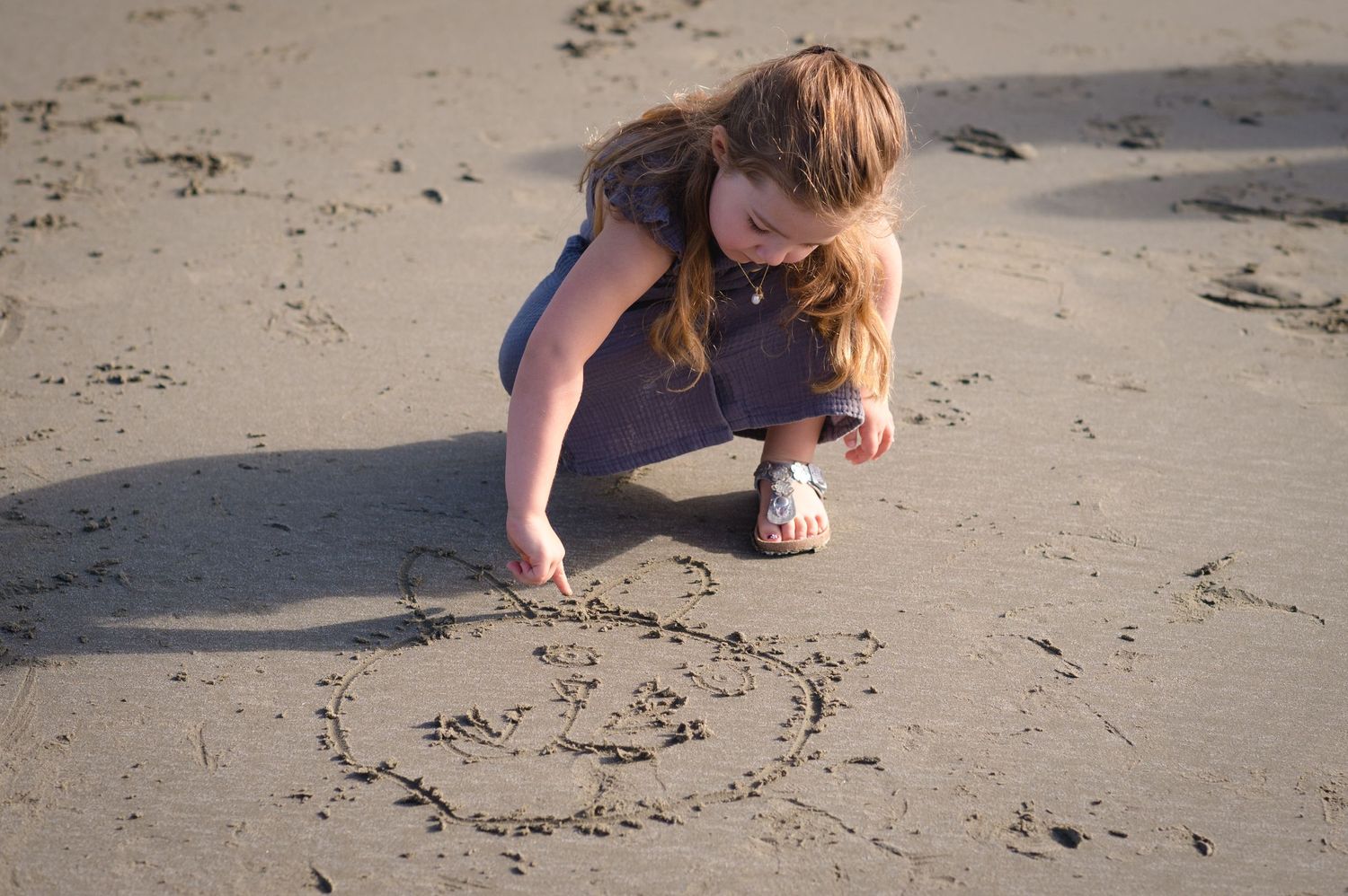 Close-up of hands drawing designs in smooth wet beach sand during sunset.