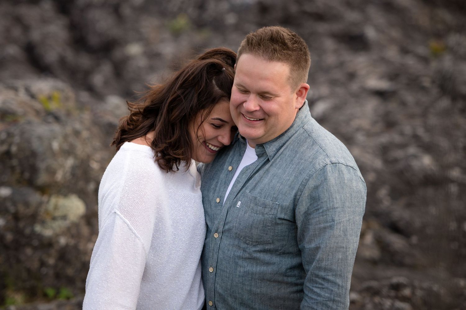 A tender moment between a couple against a backdrop of dark rocky cliffs.