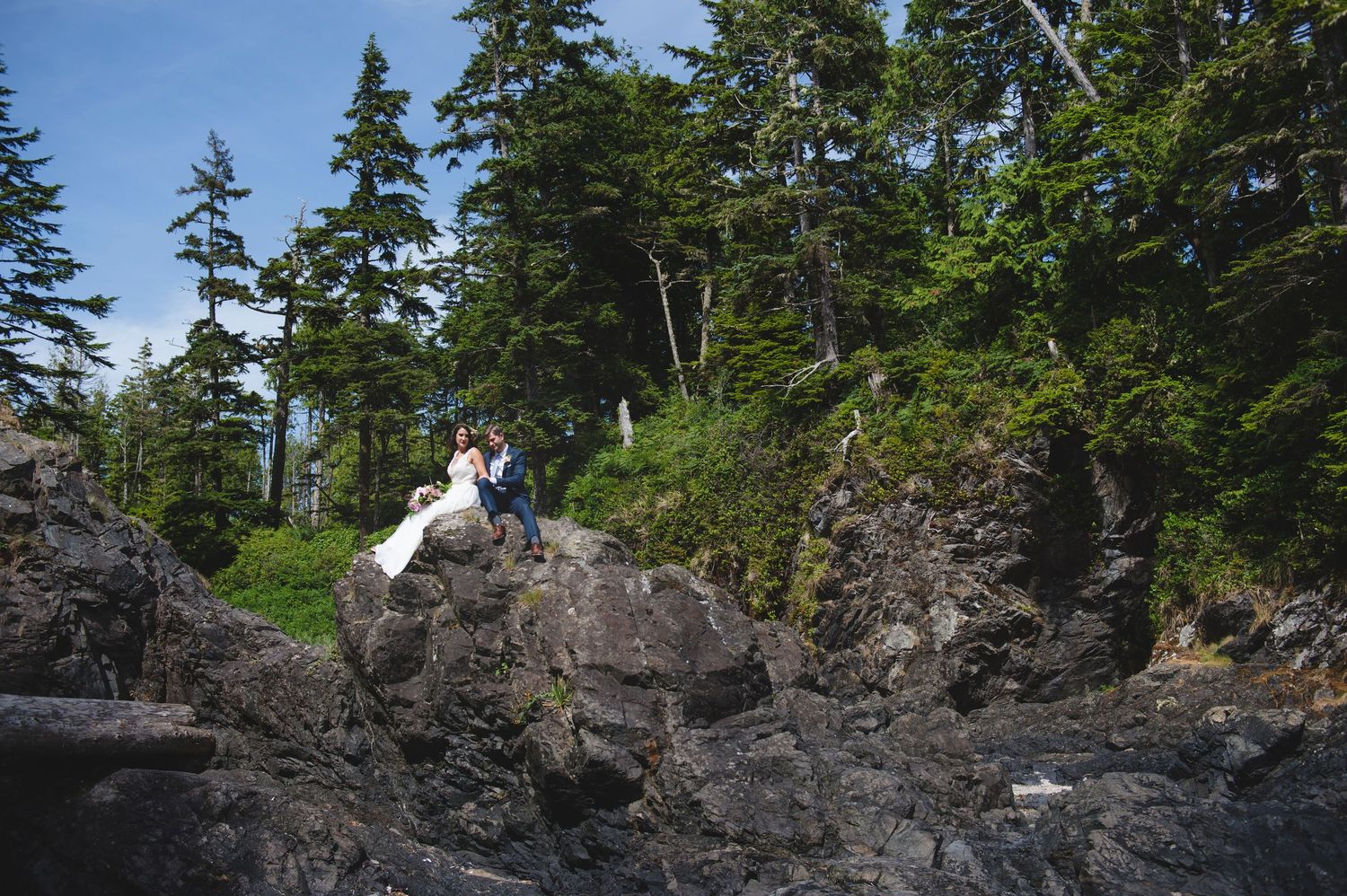 A couple sits atop dramatic black volcanic rocks along the coastline.