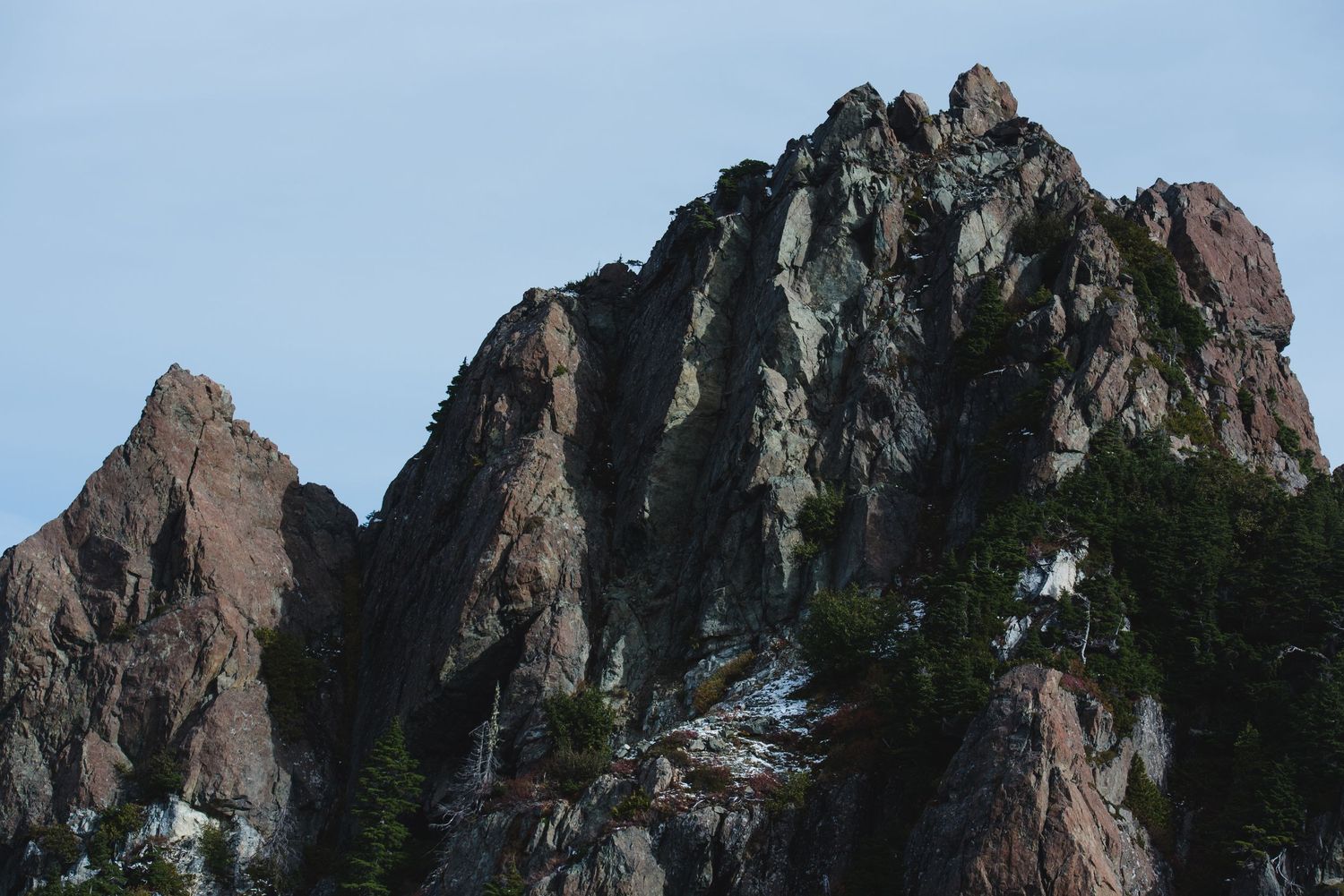 Rugged mountain cliffs rise against a blue sky with evergreen trees dotting the rocky terrain.