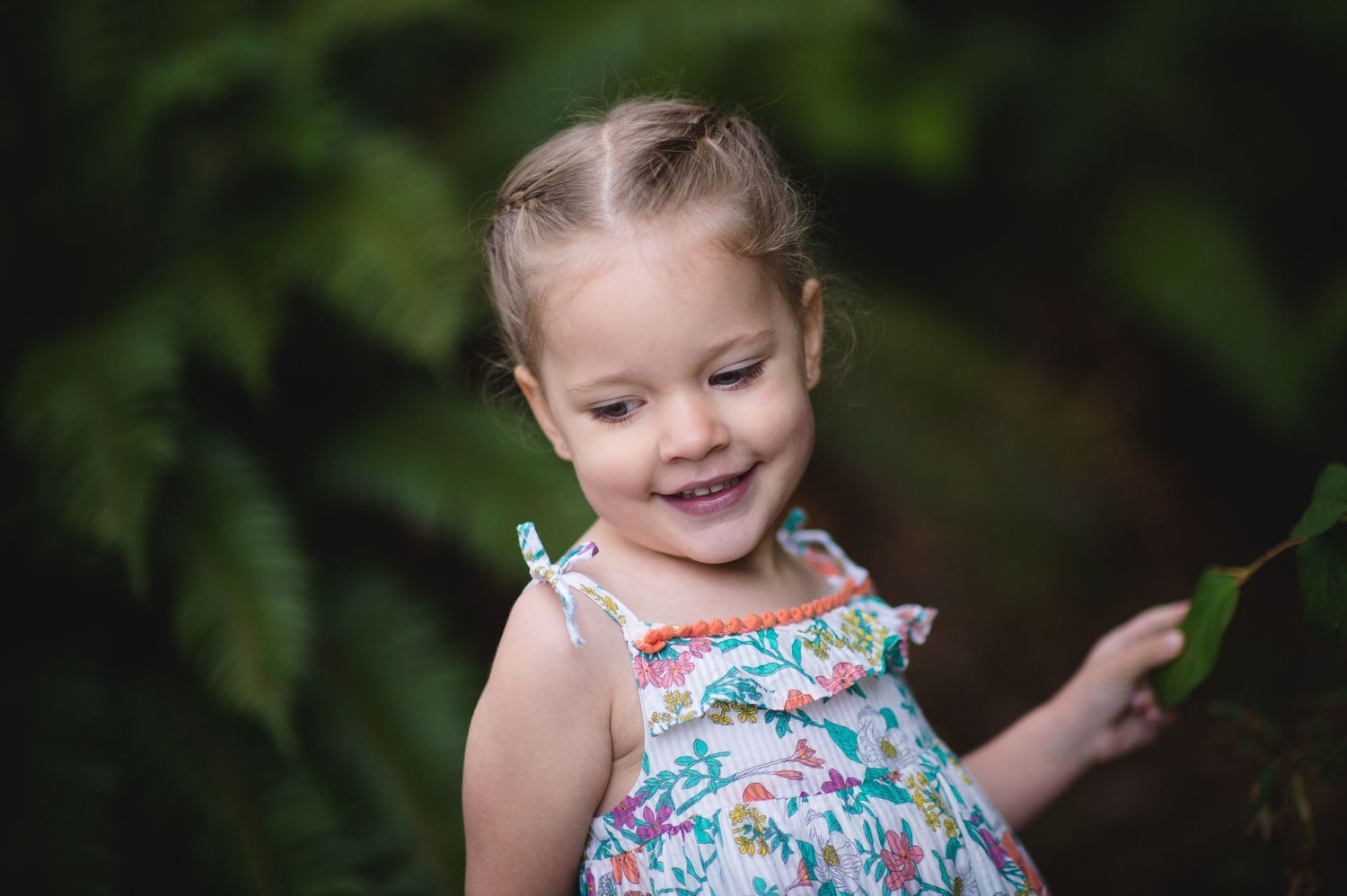 Young child in floral dress smiling while exploring outdoors.