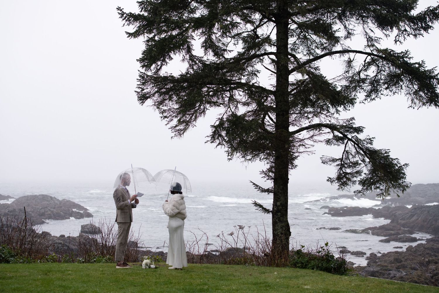 A couple stands on a cliff overlooking the rugged Pacific Ocean coastline during their outdoor wedding ceremony.