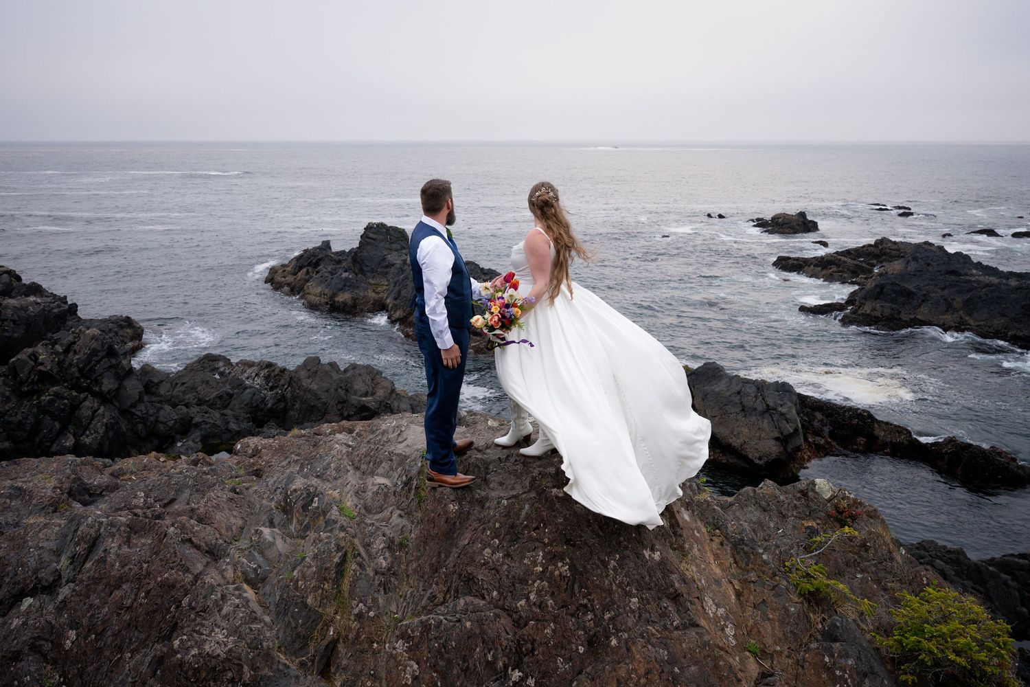 Bride and groom stand on rocky coastal cliffs in Ucluelet overlooking the ocean on their wedding day.