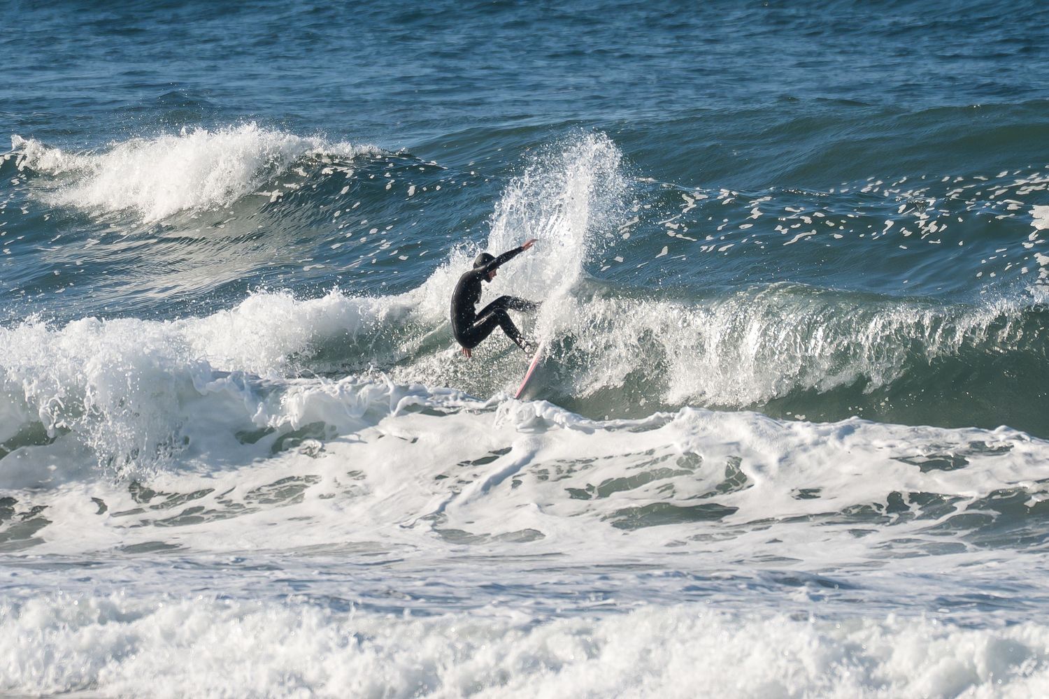 A surfer rides the crest of a breaking ocean wave with dynamic movement and white spray against blue waters.
