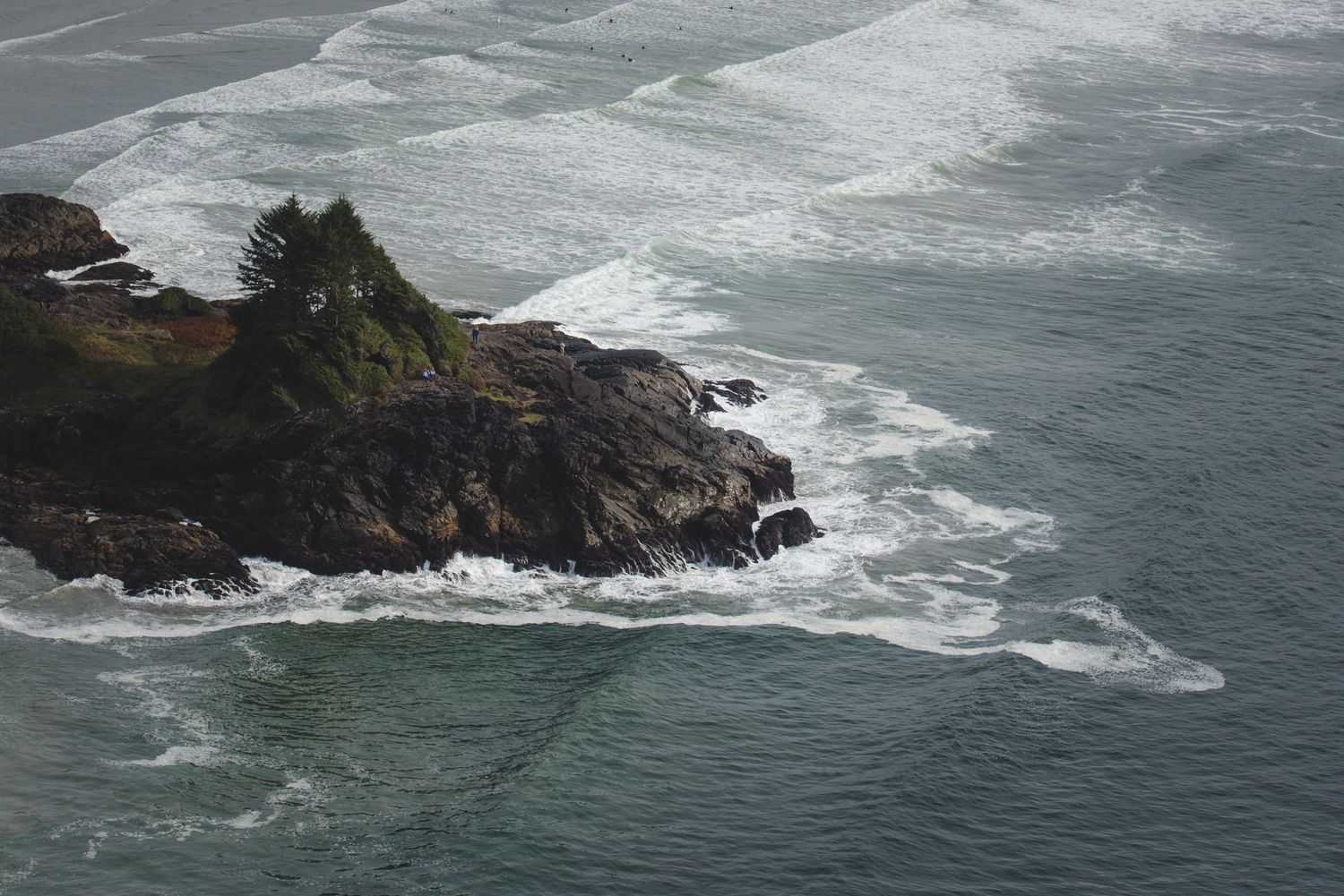 Dramatic waves crash against rocky coastal cliffs with white water patterns in the ocean.