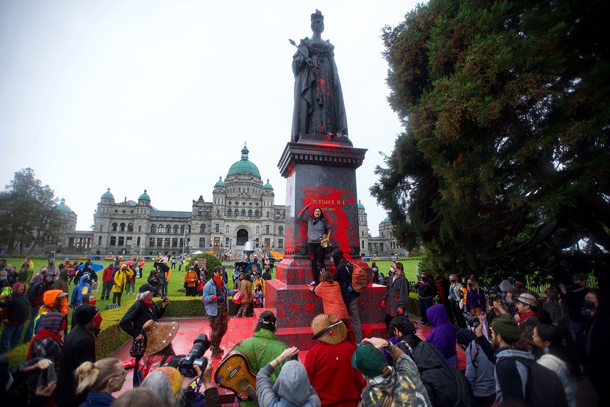 Large crowd gathering in front of historic parliament buildings with red banners and flags.