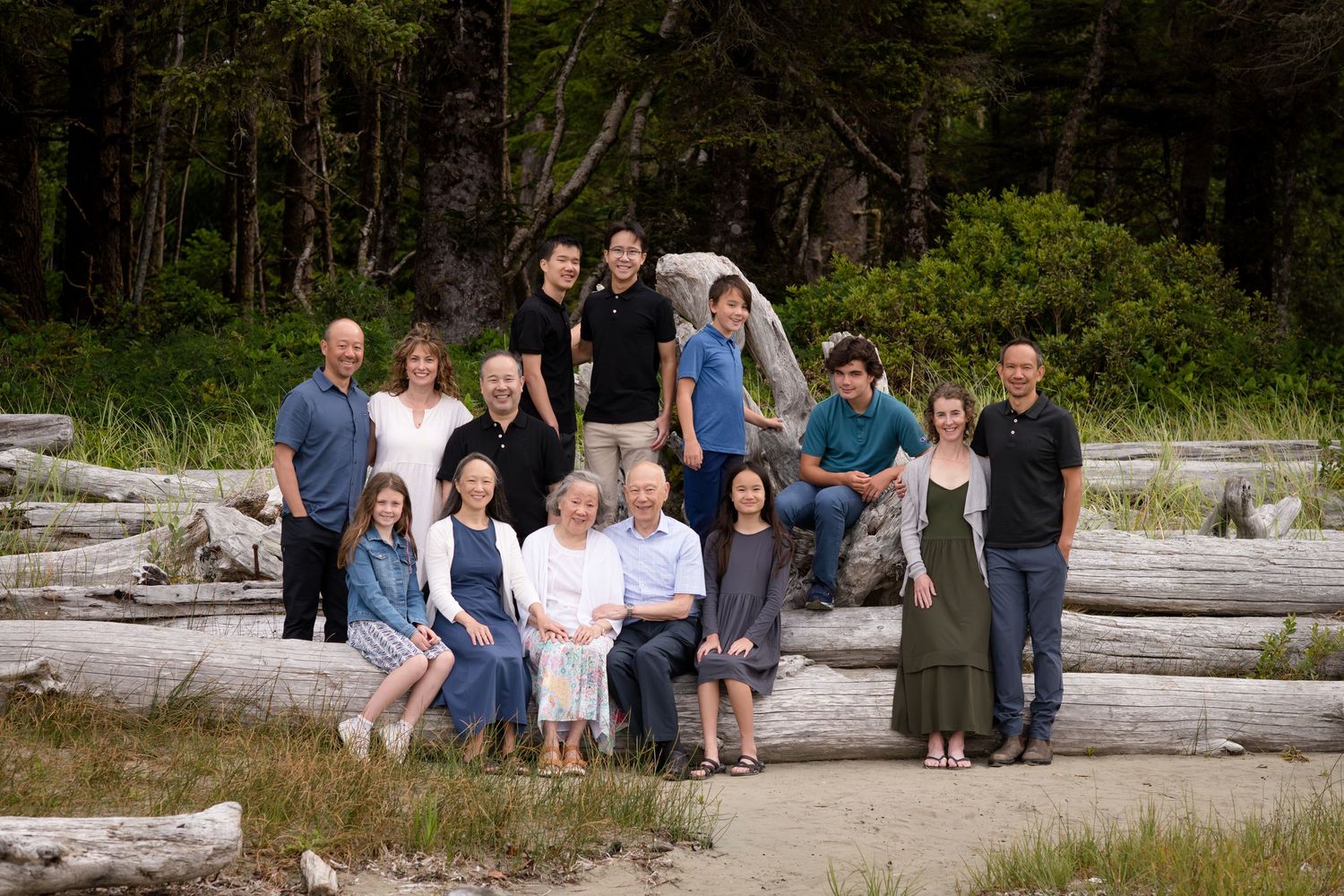 Extended family gathered on driftwood logs at the beach for a group portrait.