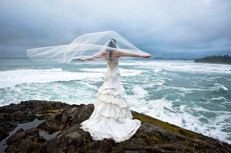 White wedding dress flowing dramatically in the wind on coastal cliffs by stormy ocean.