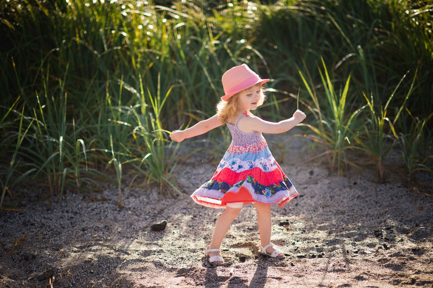 A small child in a pink dress twirls and dances joyfully in a sunlit outdoor setting.