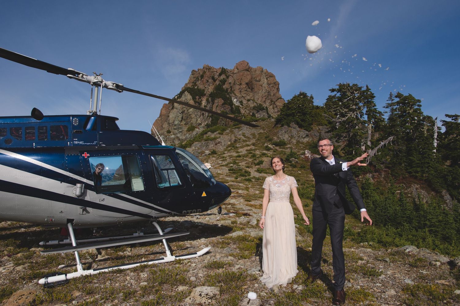 Wedding couple poses near parked helicopter on mountain summit.