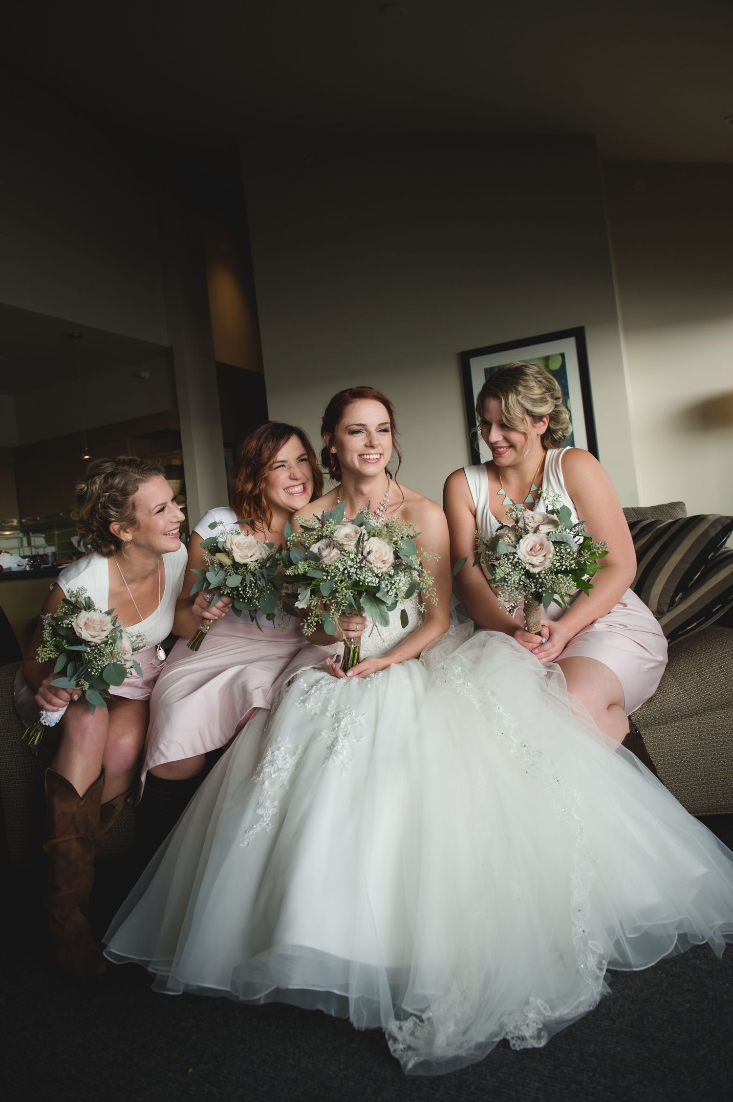 A bride in a white ballgown poses with bridesmaids wearing blush pink dresses while holding floral bouquets.
