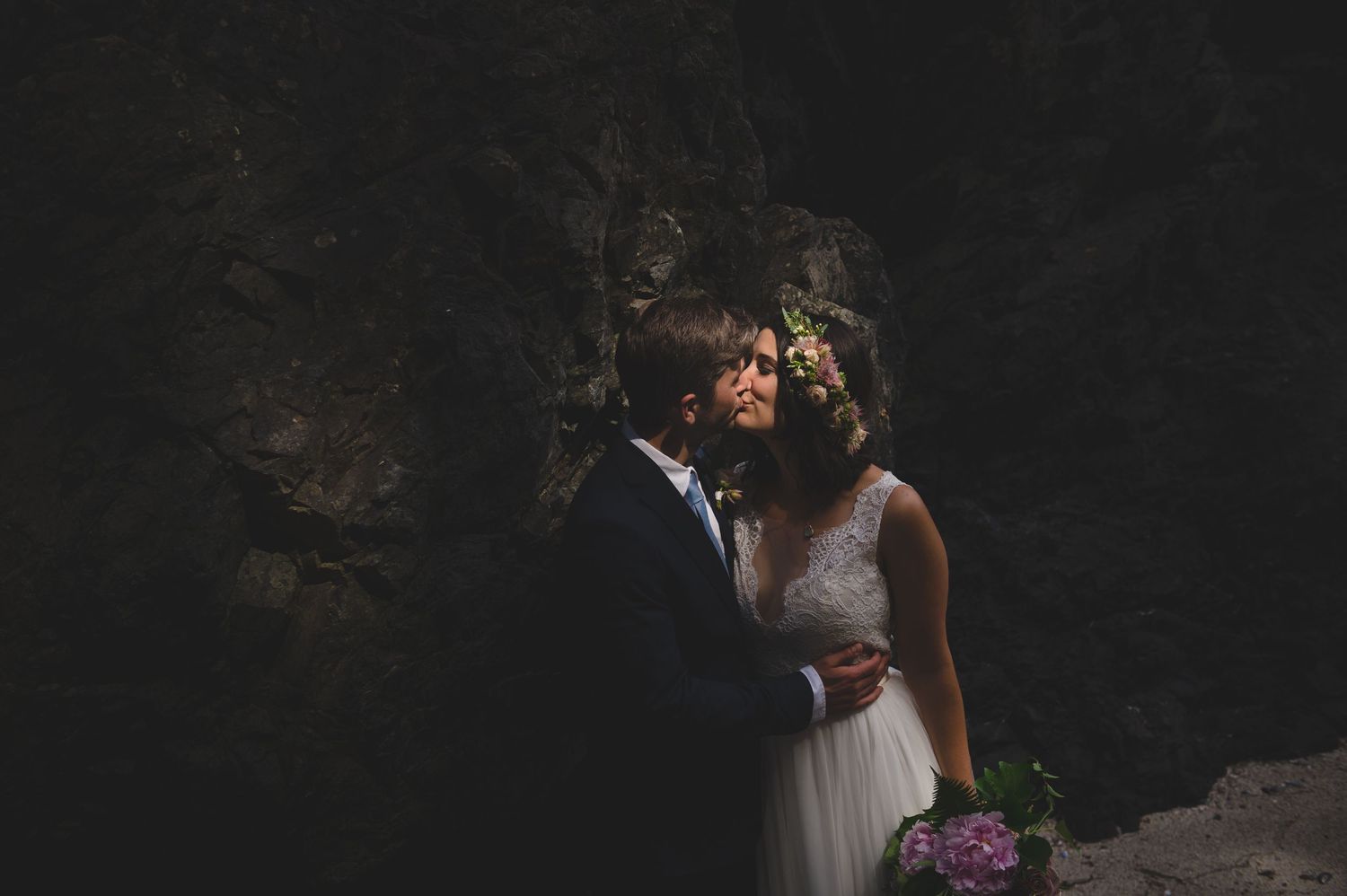 Wedding couple embracing on rocky coastal cliffs at sunset.