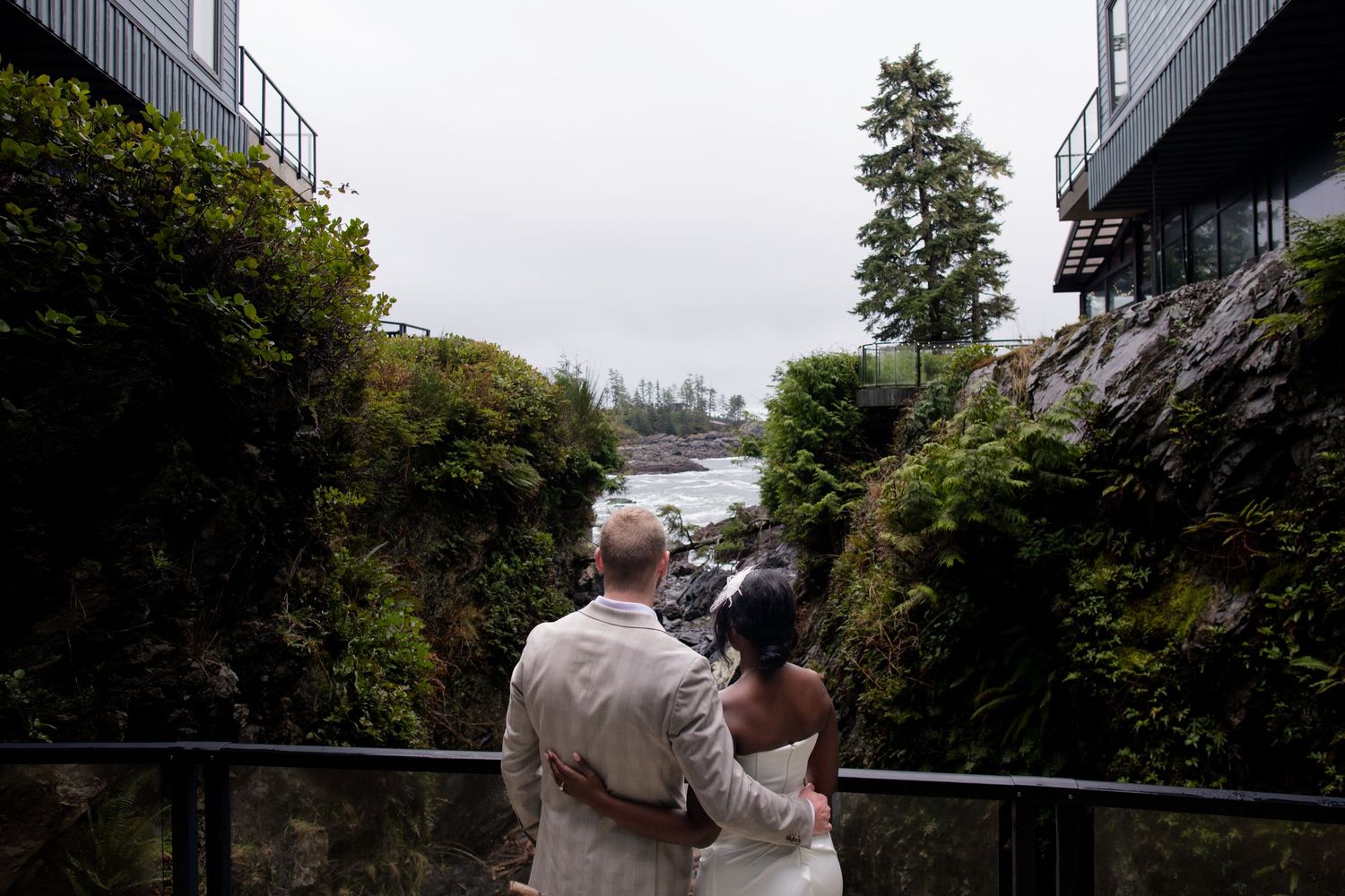 A couple enjoys a romantic moment on a balcony overlooking a scenic landscape with trees and buildings.