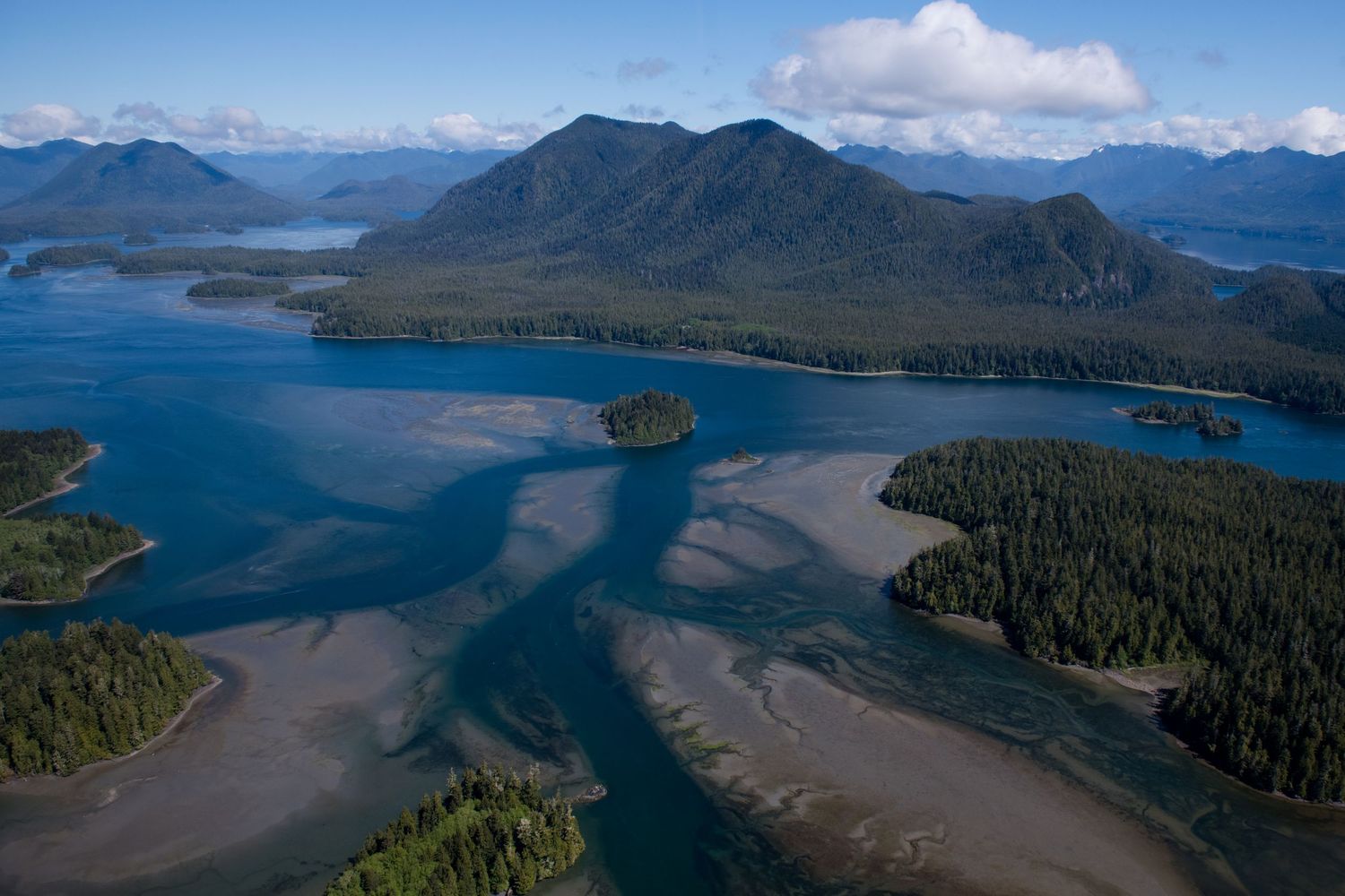 Aerial panorama of a rugged coastline with forested islands and mountains rising from pristine blue waters.