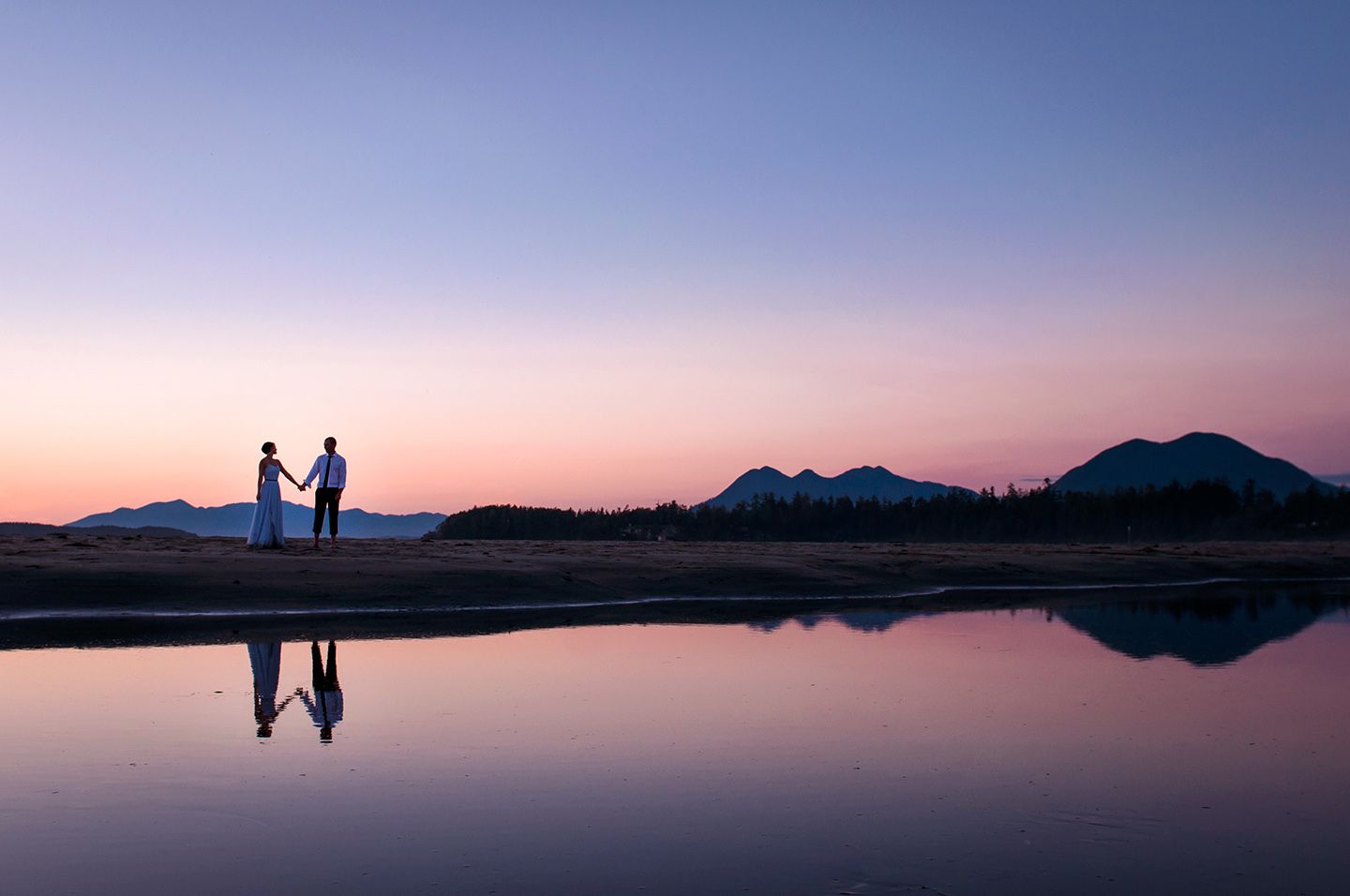 Silhouettes against sunset sky with mountains and water creating dramatic panoramic view.