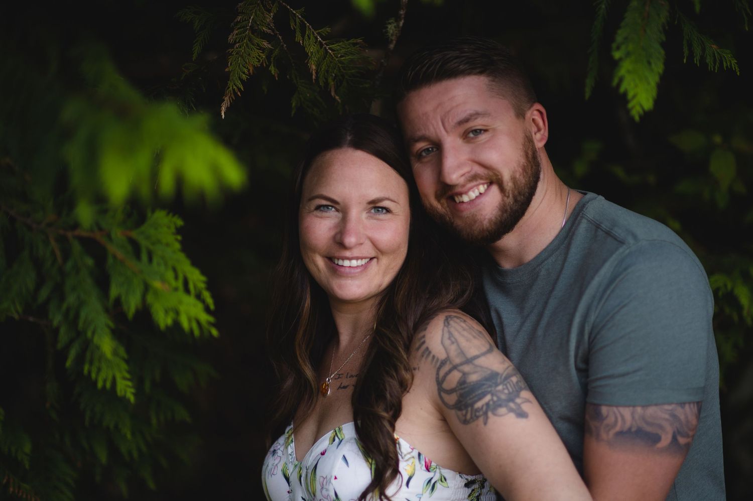 A romantic couple embraces under evergreen trees in a forest setting.