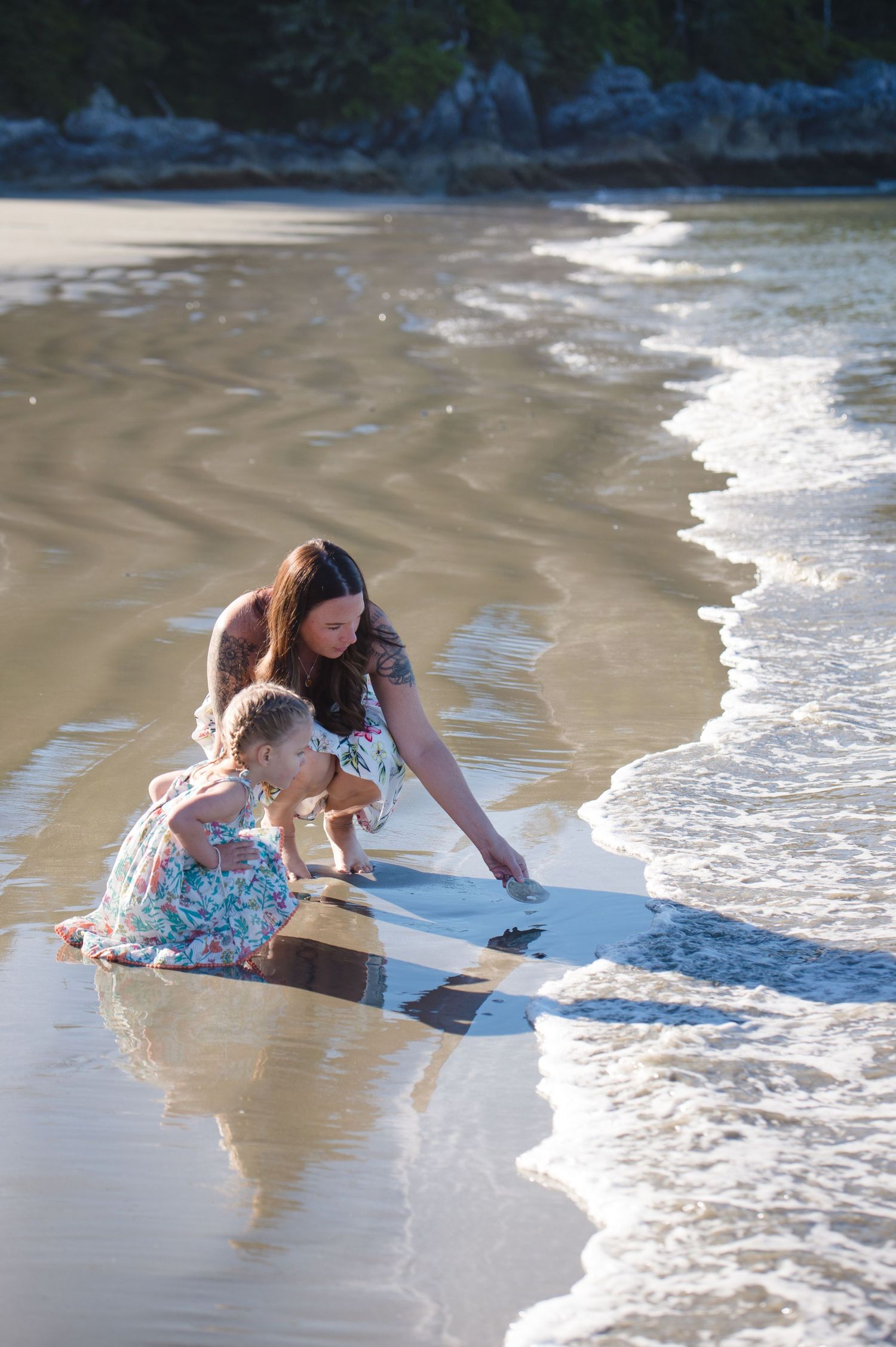 People playing in gentle ocean waves on sandy beach during summer day.