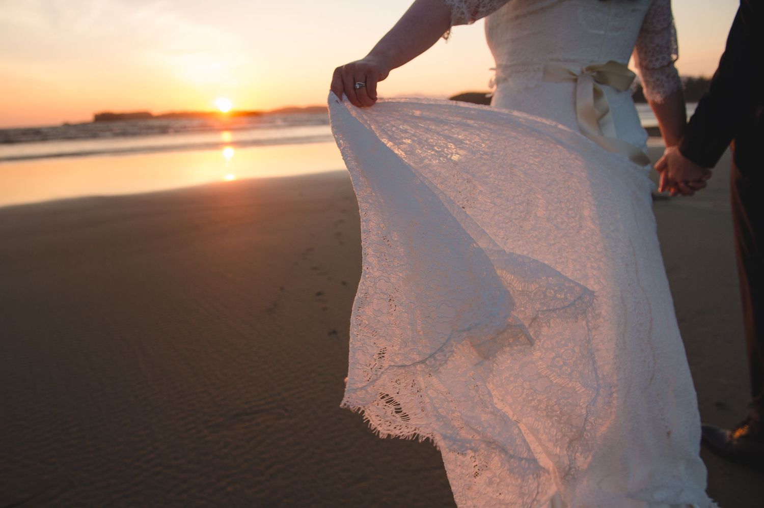 White lace wedding dress fabric flows in the wind during sunset on a beach.