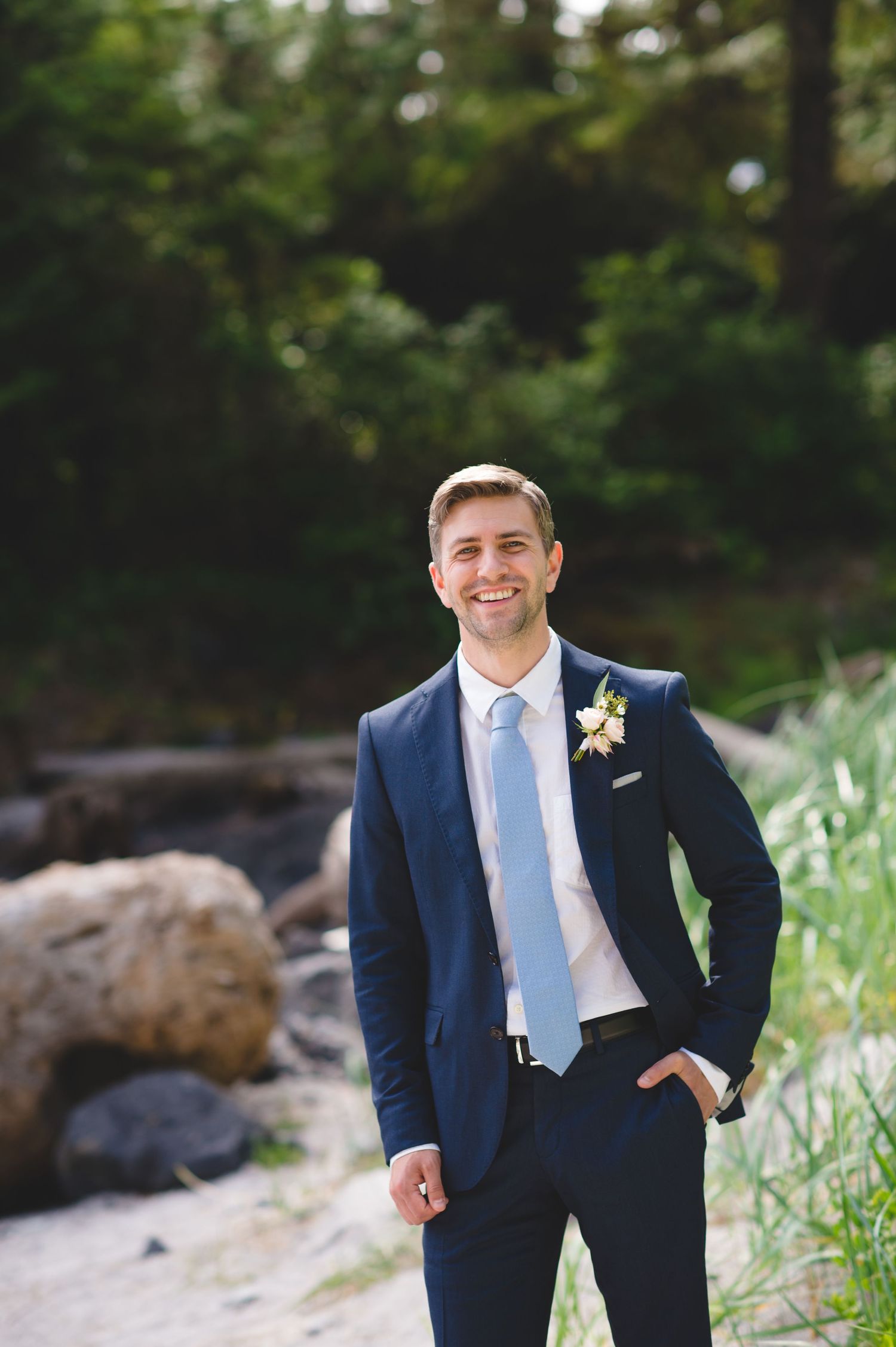 Wedding portrait in navy suit and light blue tie against natural outdoor backdrop.