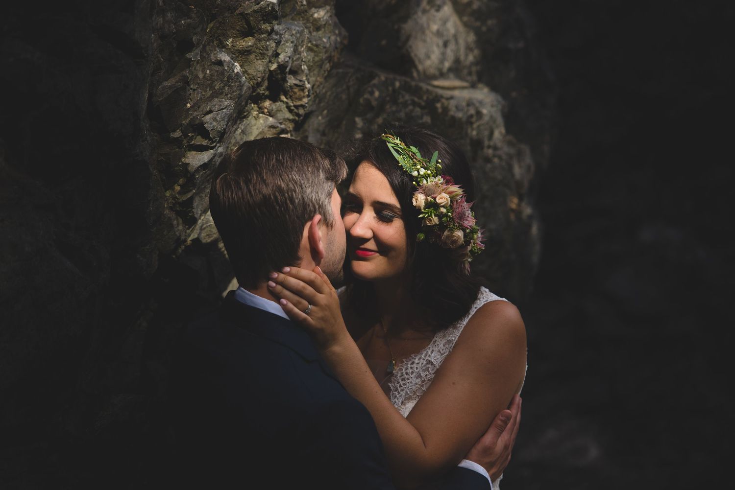 Romantic wedding portrait against dark rocky backdrop.