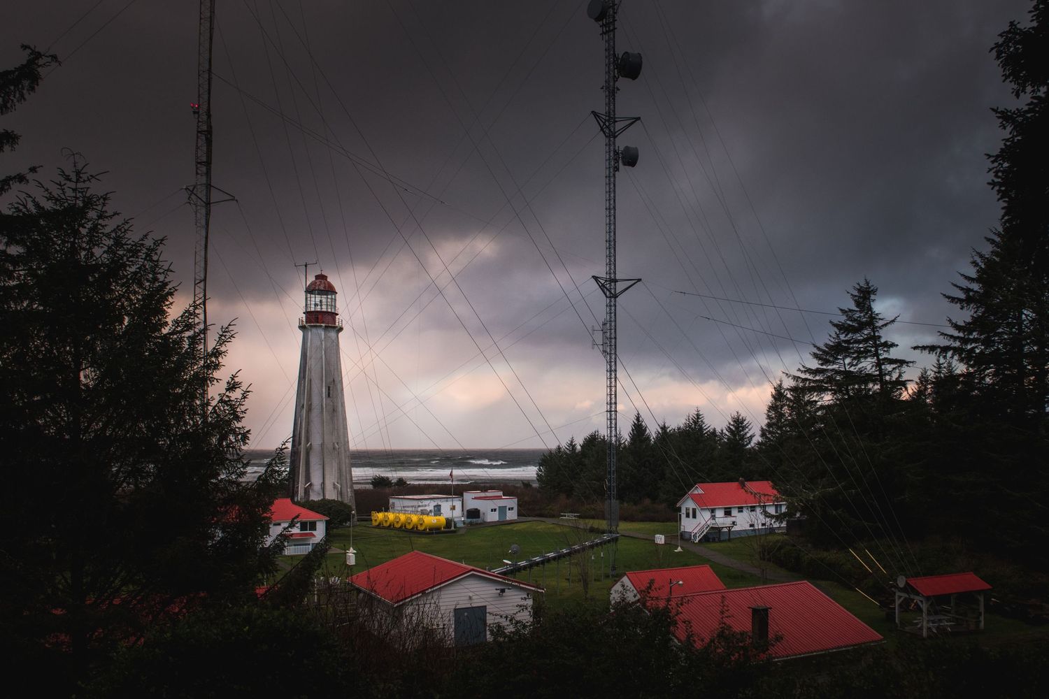 Lighthouse station with red buildings under dramatic stormy skies.