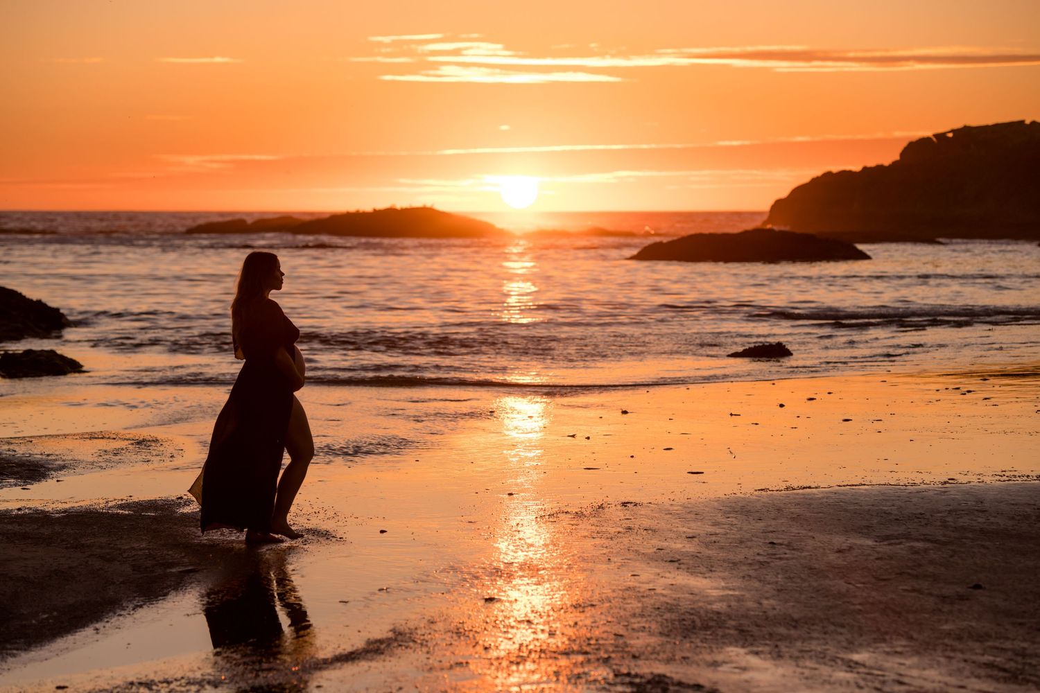 Dramatic orange sunset over a rocky coastline with waves crashing against the shore.