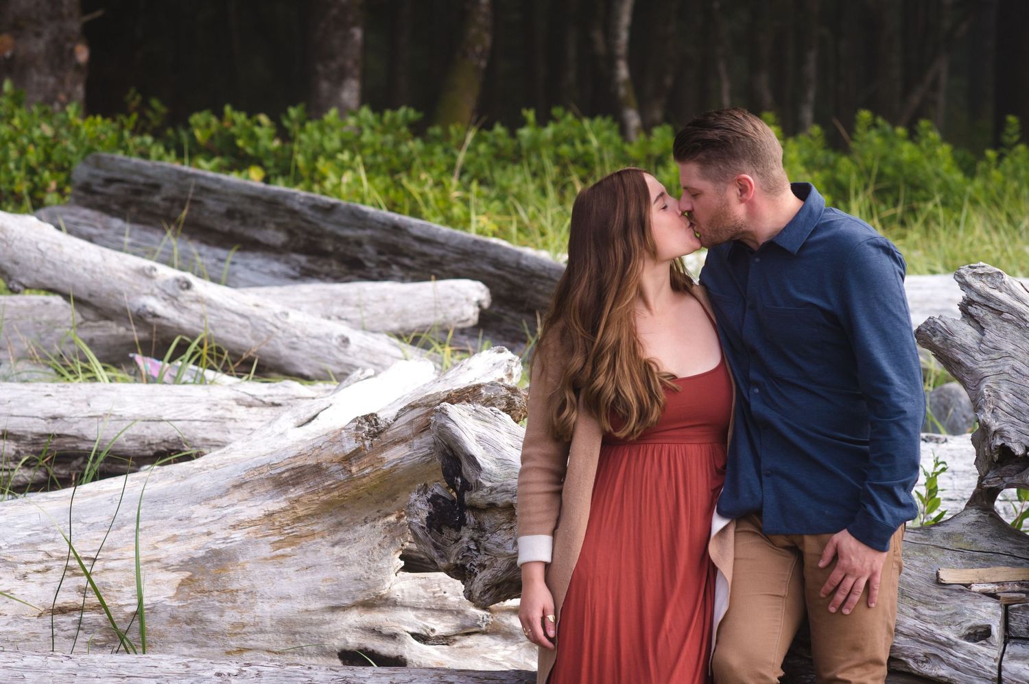 An intimate moment between a couple on driftwood at the beach.