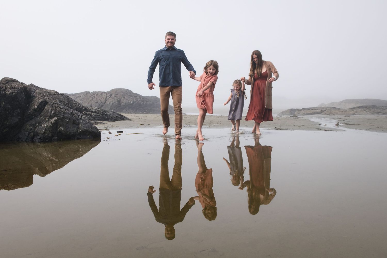 People walking together on scenic beach with mountain backdrop and mirror-like sand reflections.