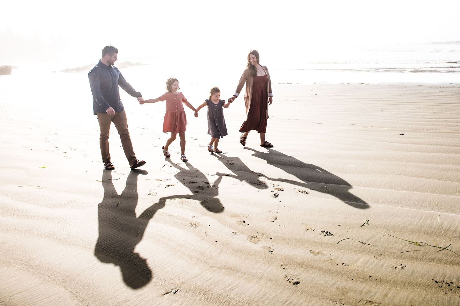 Shadows cast on sandy beach as family walks together at sunset.