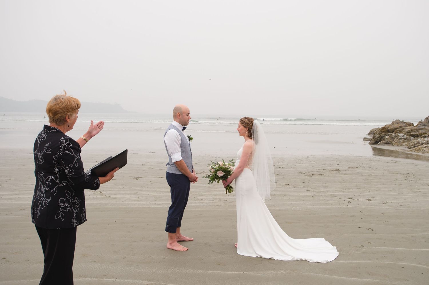 A wedding ceremony takes place on a misty beach with waves in the background.