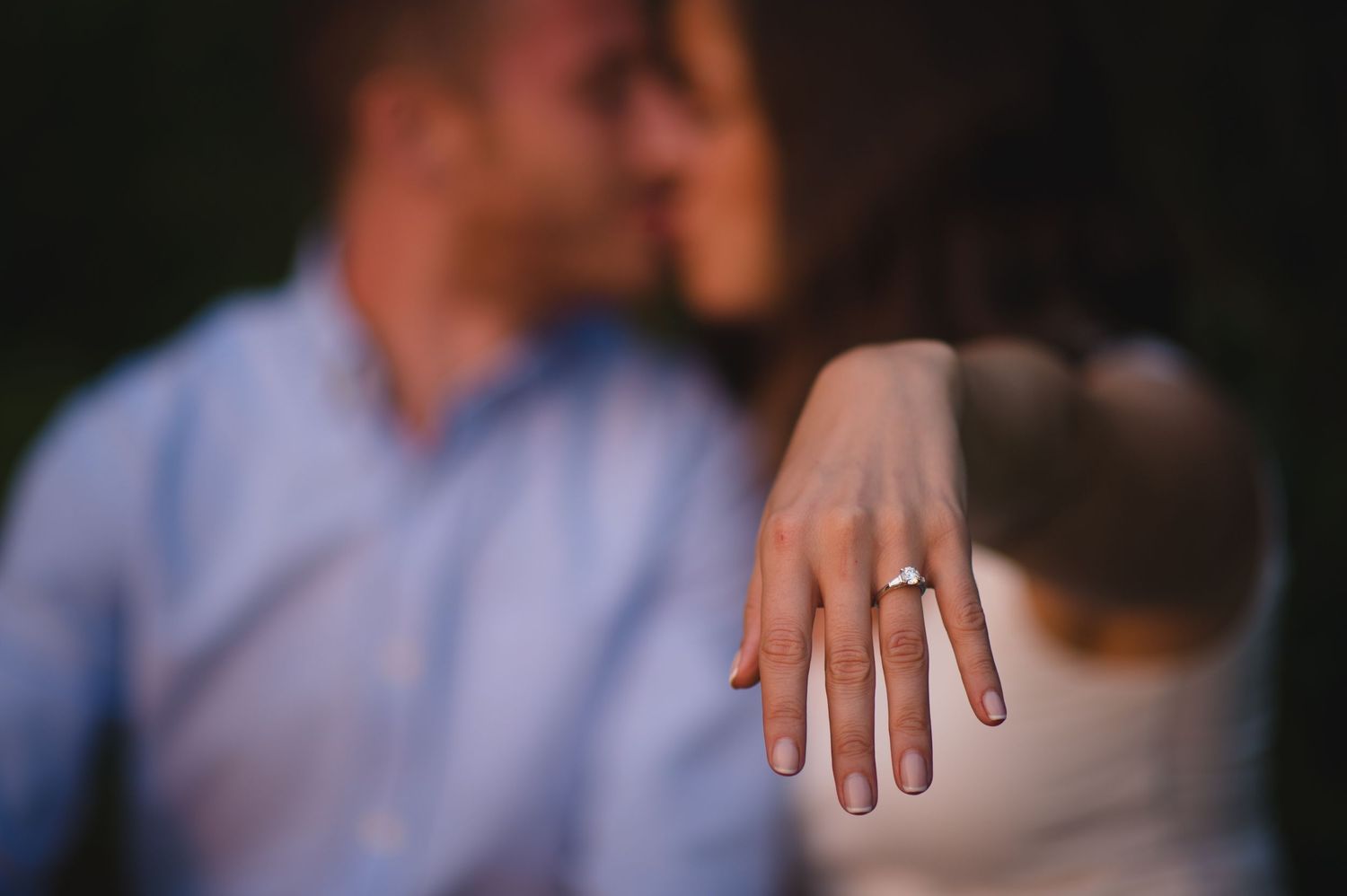 Close-up shot of hands with an engagement ring against a soft blurred background.