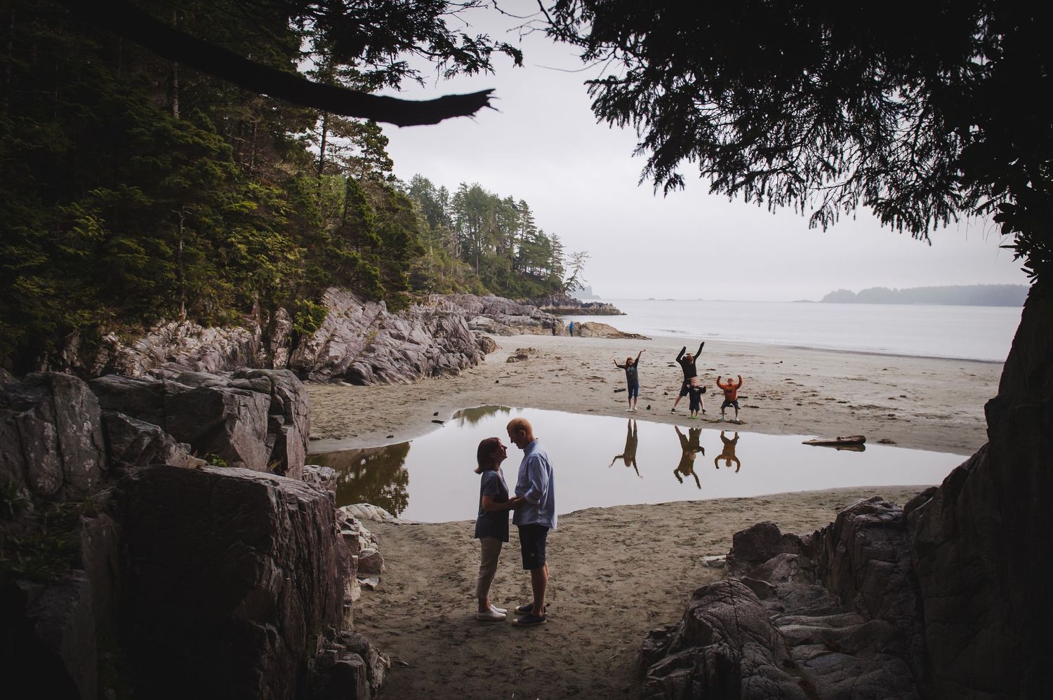 Beach scene through cave opening with people playing in distance at low tide.