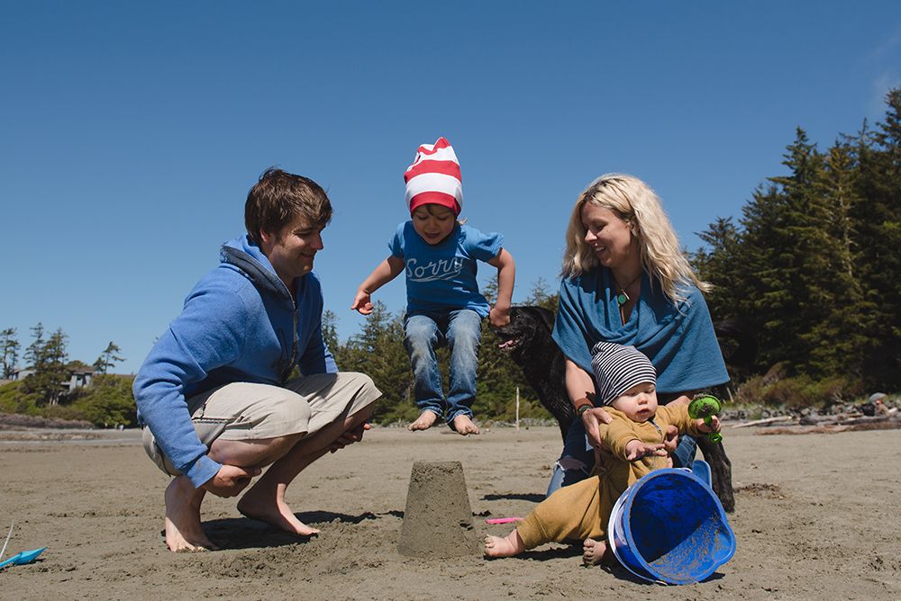 Three people enjoying a sunny day at the beach with sand toys and blue sky overhead.