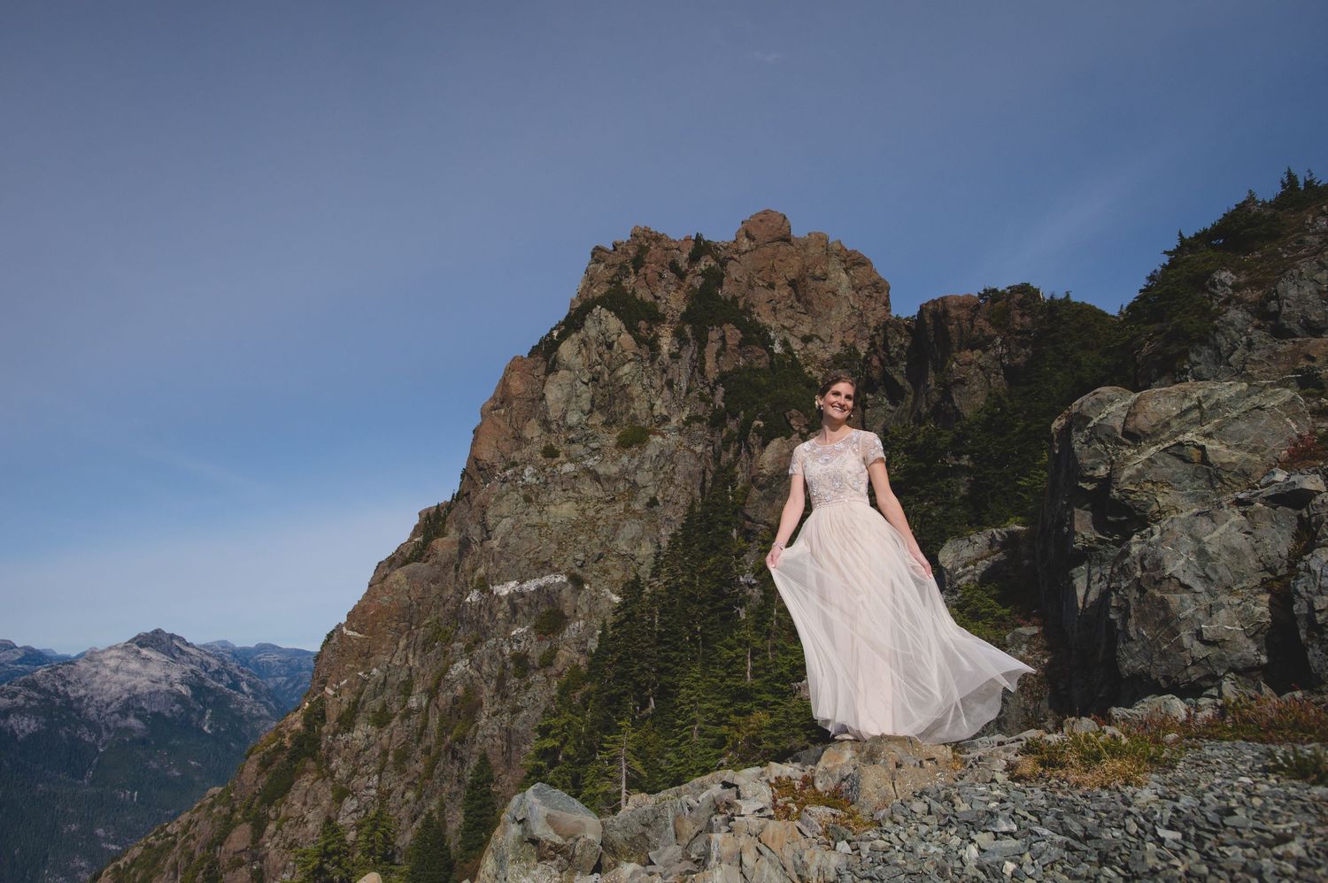 Flowing dress catches the wind against rugged mountain landscape and blue sky.