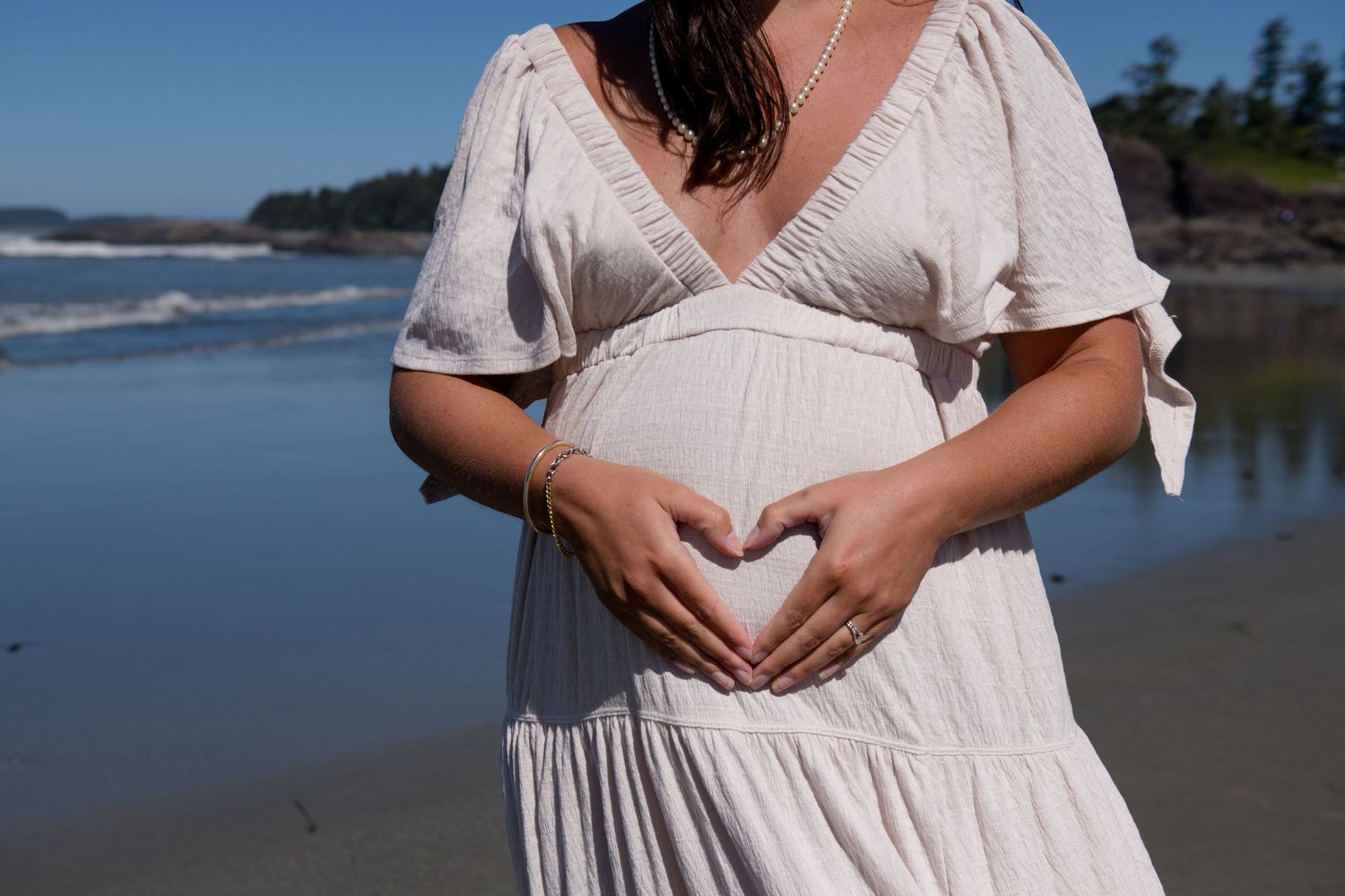 Close-up details of a flowing white maternity dress against coastal backdrop.