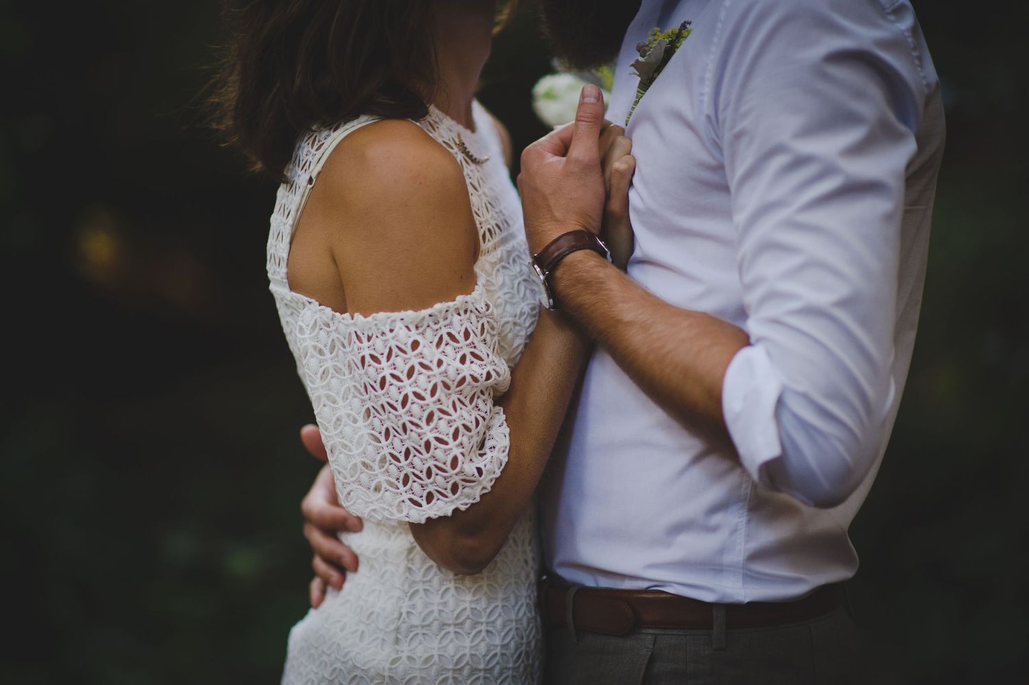 Romantic couple in white attire embracing on beach during sunset photoshoot.