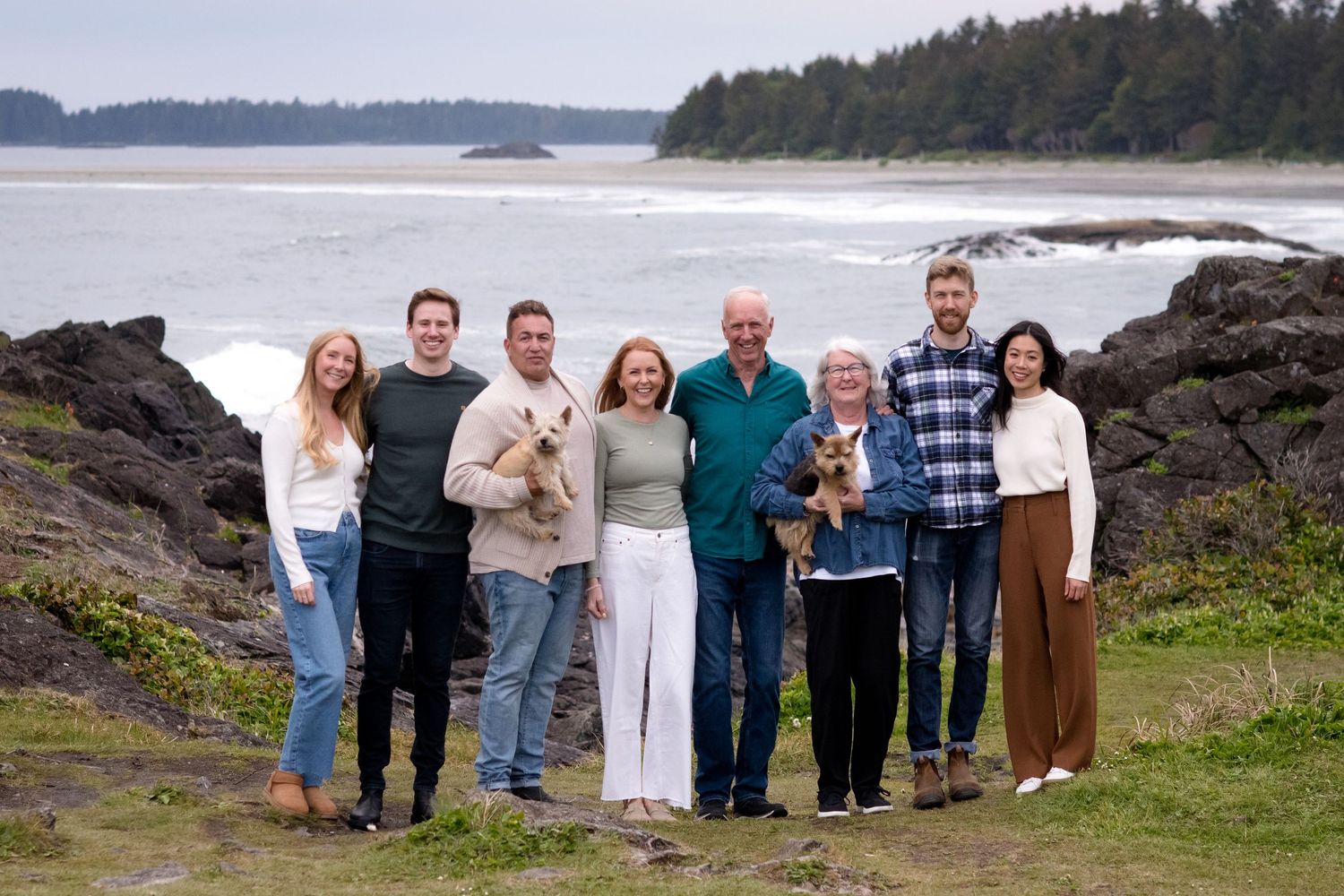 A group stands together on a rocky coastal cliff overlooking the Pacific Ocean with evergreen trees in background.