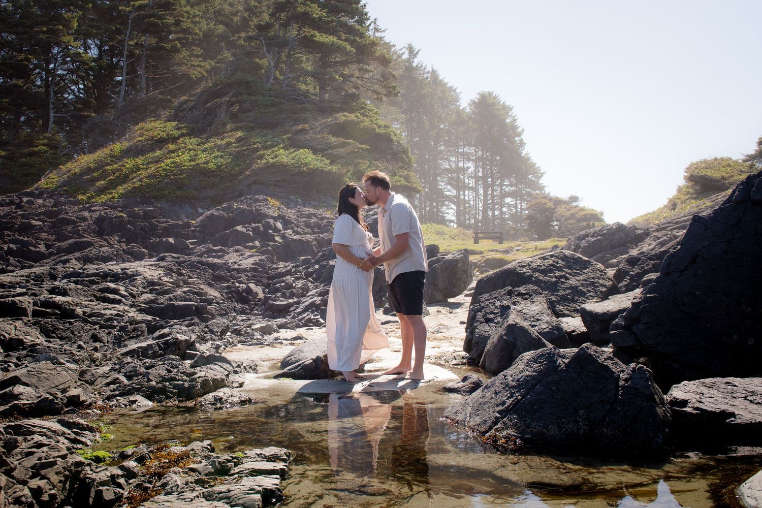 Scenic coastal maternity photos taken among mossy rocks and evergreen trees.