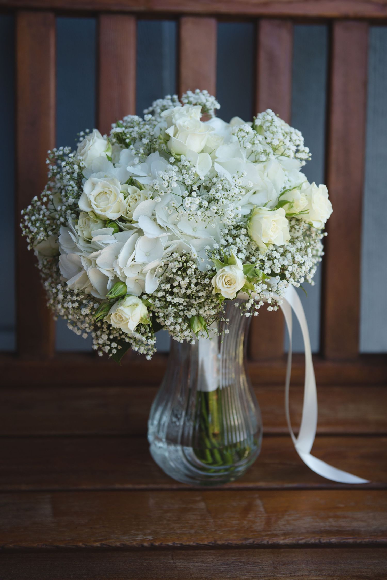 White roses and baby's breath bouquets in glass vases with ribbon accents.