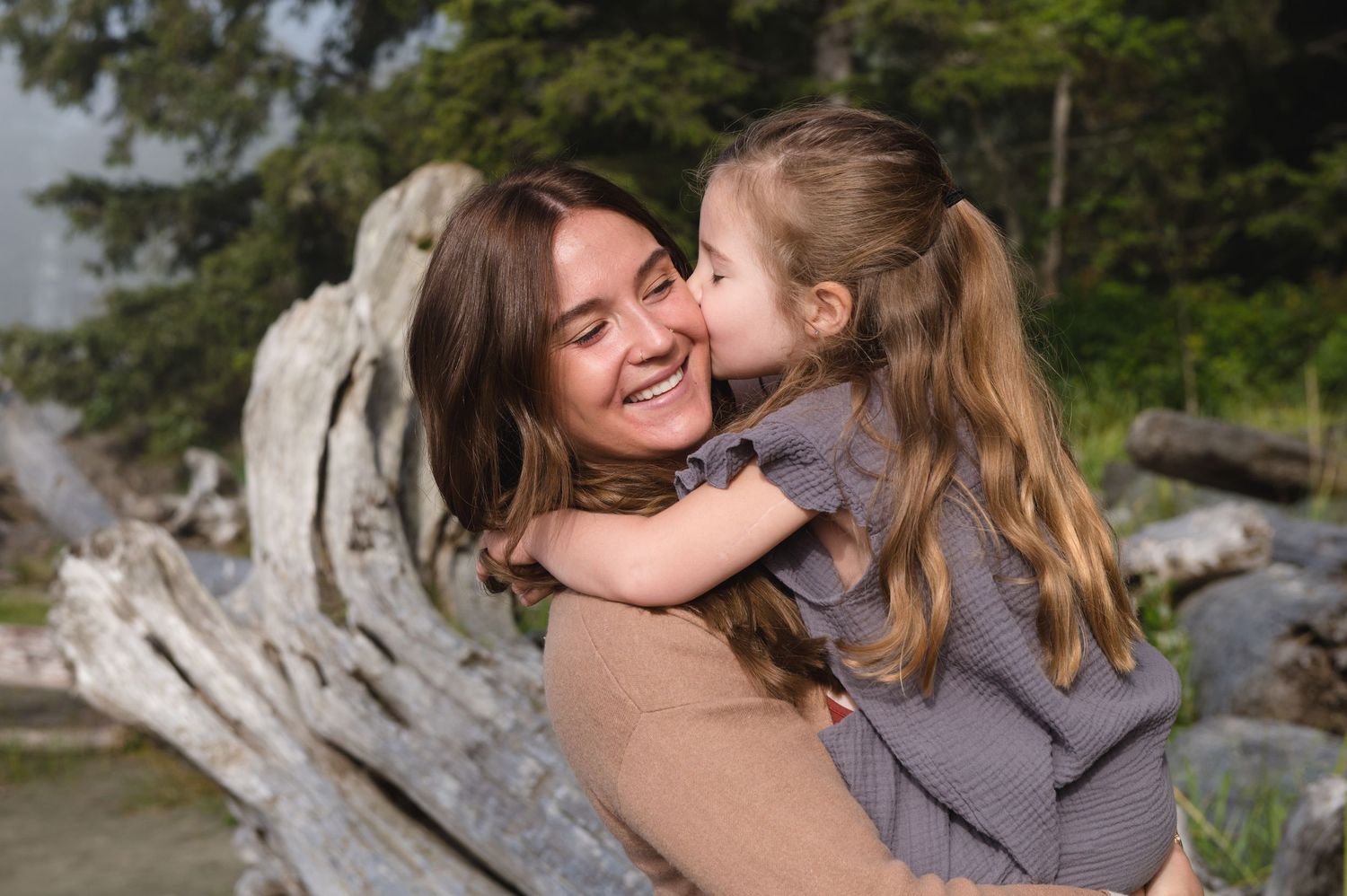 A tender embrace shared between two people on a driftwood-strewn beach.