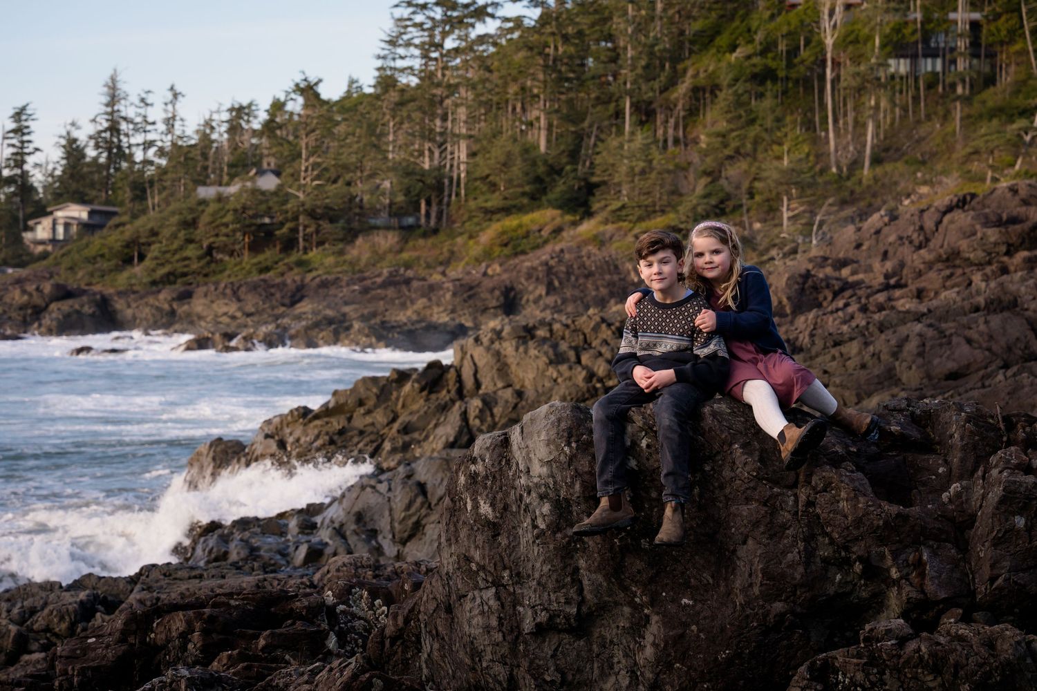 Coastal landscape with people sitting on rocky cliffs overlooking Pacific ocean waves.