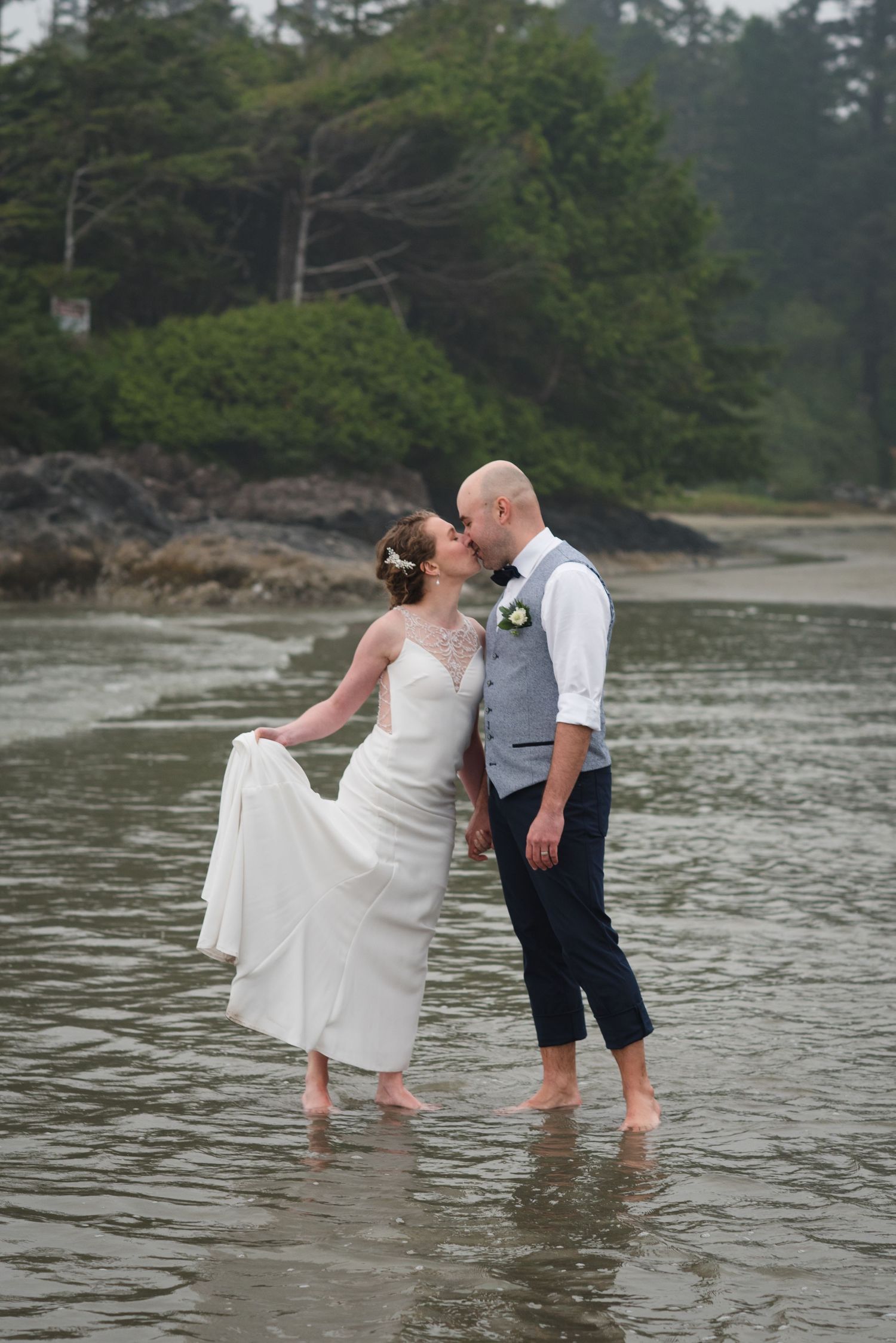 A couple wades through shallow coastal waters during their beach wedding photoshoot.