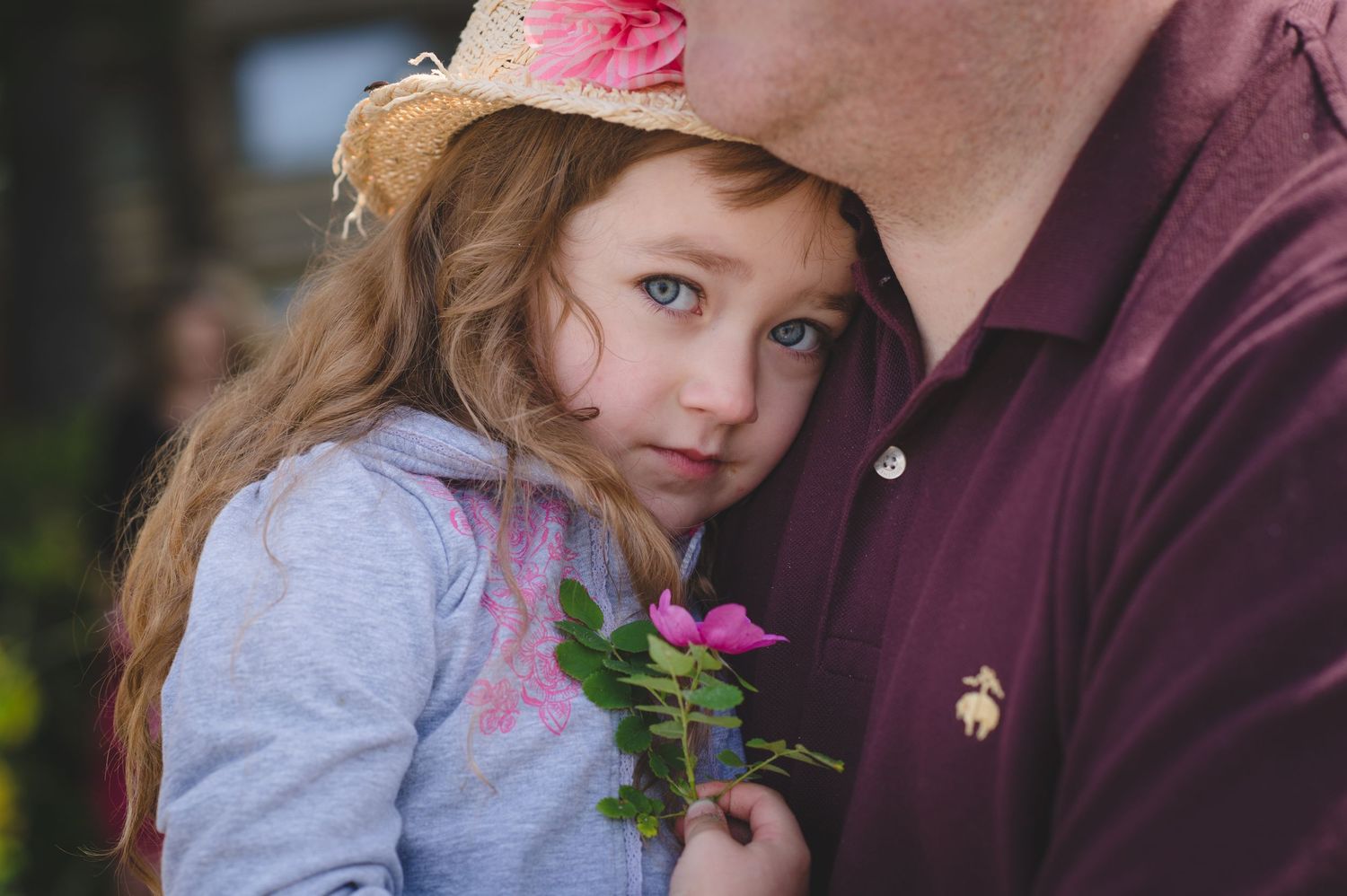 Child holding pink flowers while wearing gray clothing against a purple background.