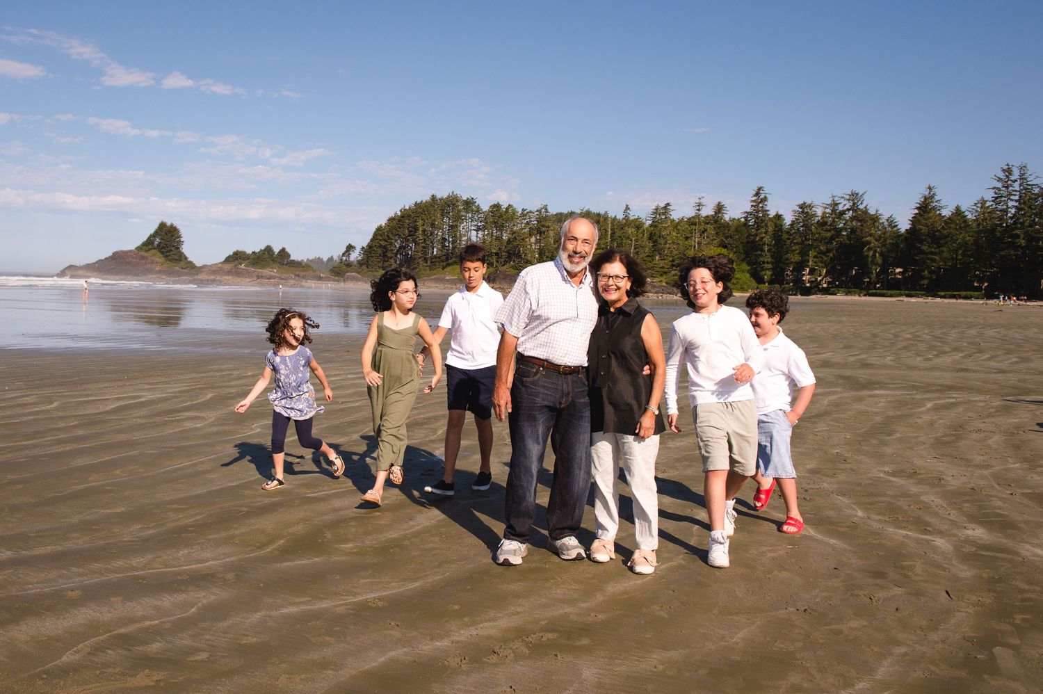 A group of people walking together on a sandy beach with trees and rock formations in the background.