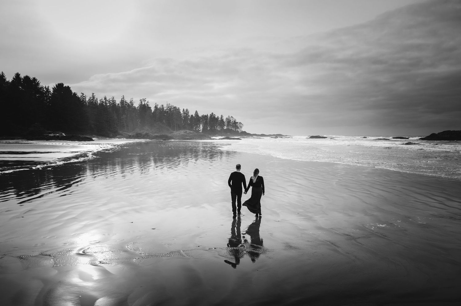 Black and white silhouettes of couple walking along misty beach at sunset.