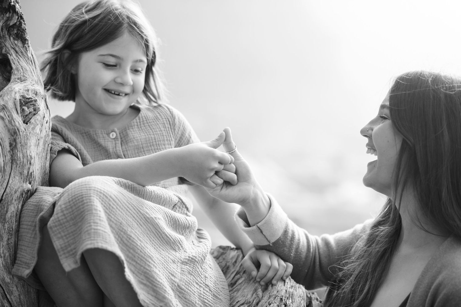 A playful black and white moment of laughter and connection on a tree trunk.