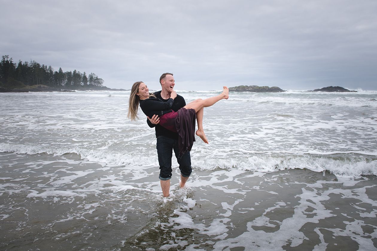People playing in ocean waves along dramatic Pacific Northwest coastline.