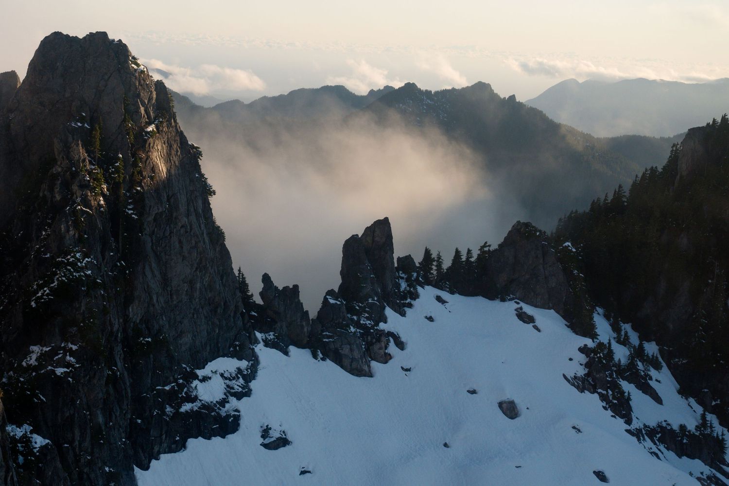 Dramatic aerial view of jagged snow-covered mountain peaks with misty clouds rolling through the rocky valleys.
