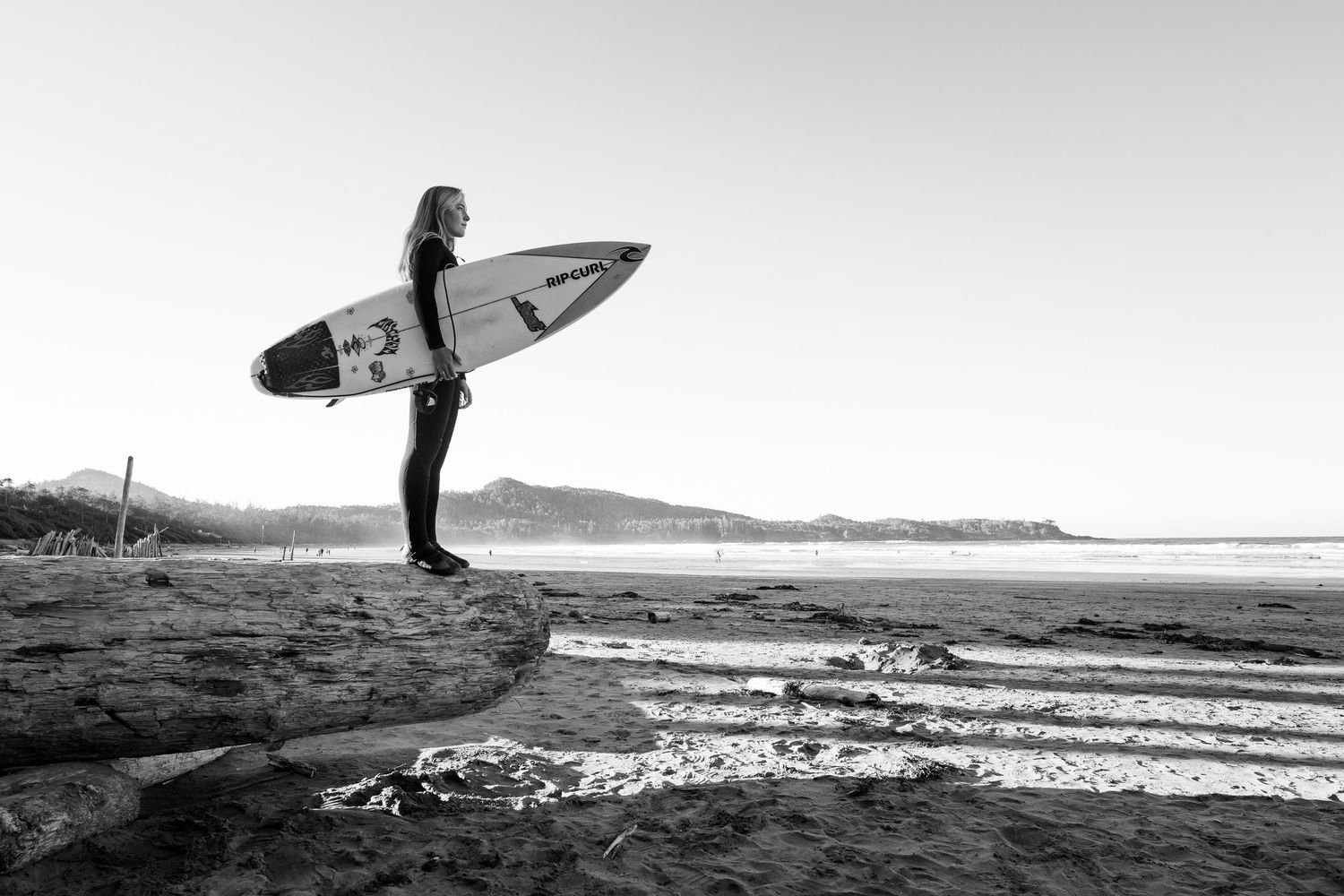 A series of black and white photos showing surfers carrying boards along a scenic beach shoreline.
