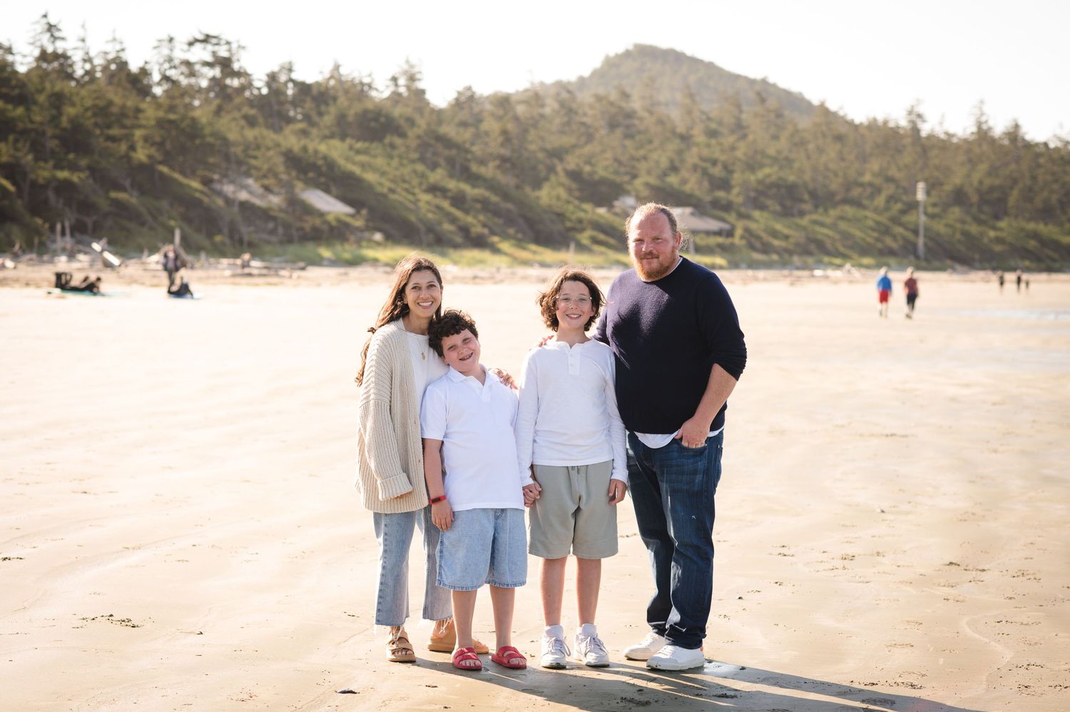 Family walking together on a scenic beach with mountains and trees in the background during sunset.
